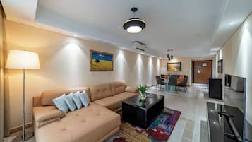 A modern living room with a sofa, coffee table, and a TV. There is a dining area with chairs and a table in the background.