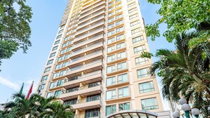 A tall hotel with multiple floors, a glass entrance, and a landscaped entrance area with palm trees and plants.