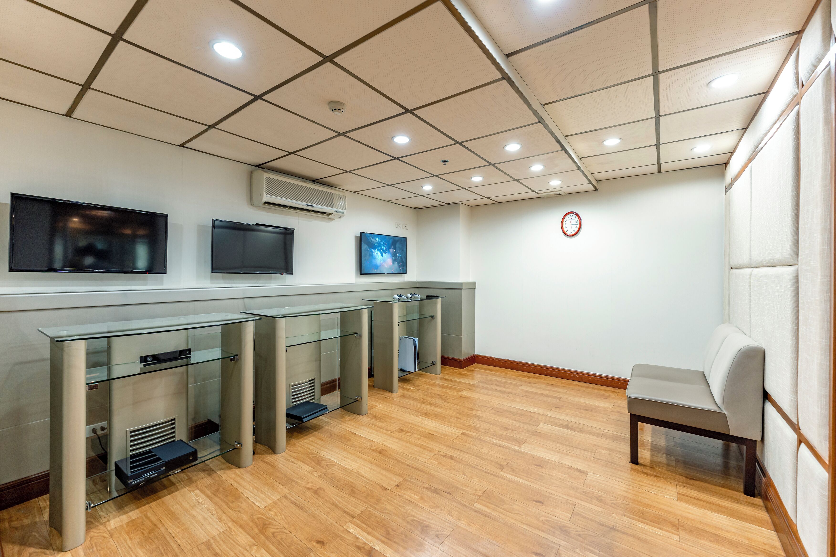 Een moderne hotellobby met een receptiebalie, flatschermtelevisies, een klok en een zithoek.