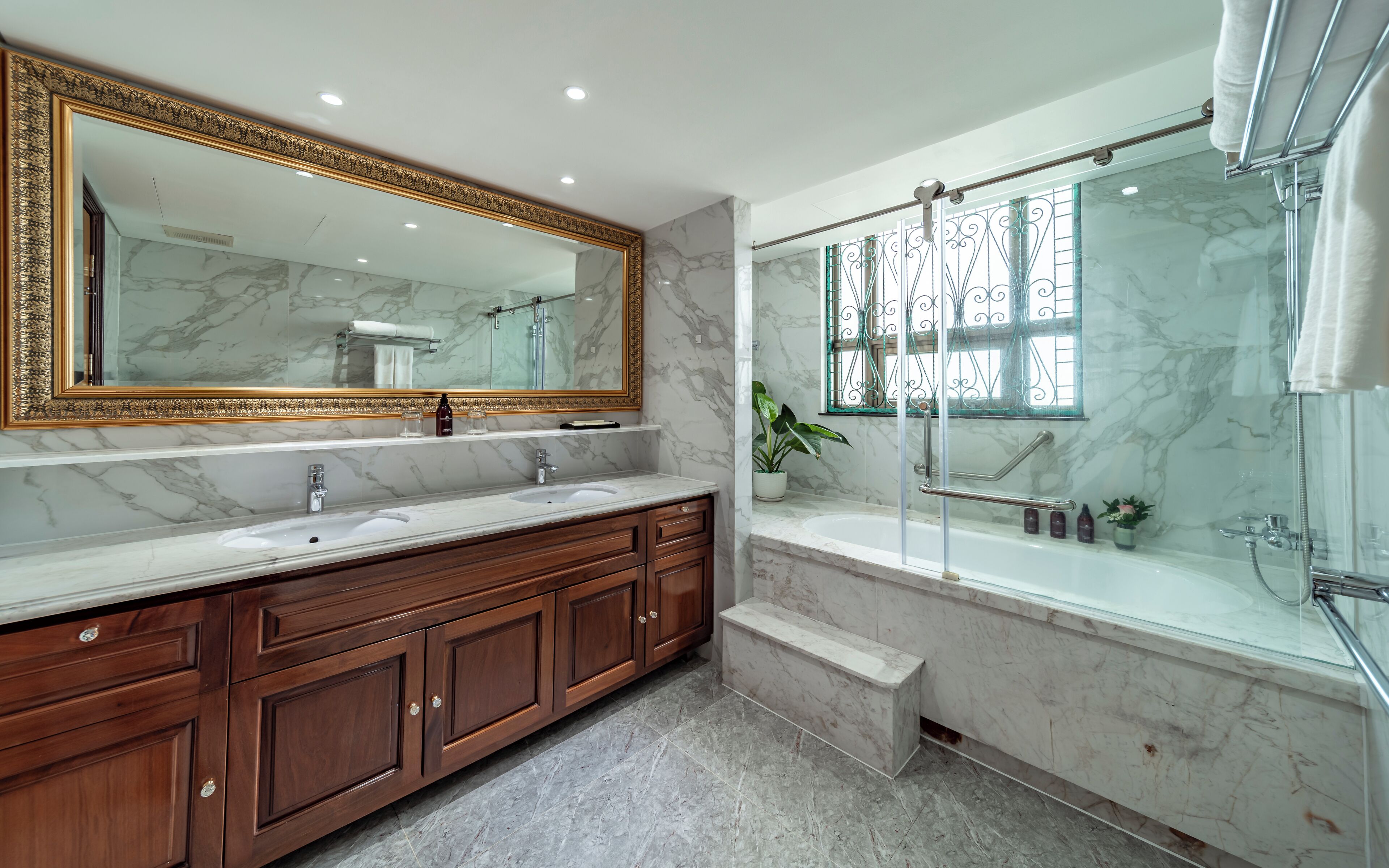 A bathroom with a marble vanity, a large mirror, a shower with glass doors, and a potted plant.