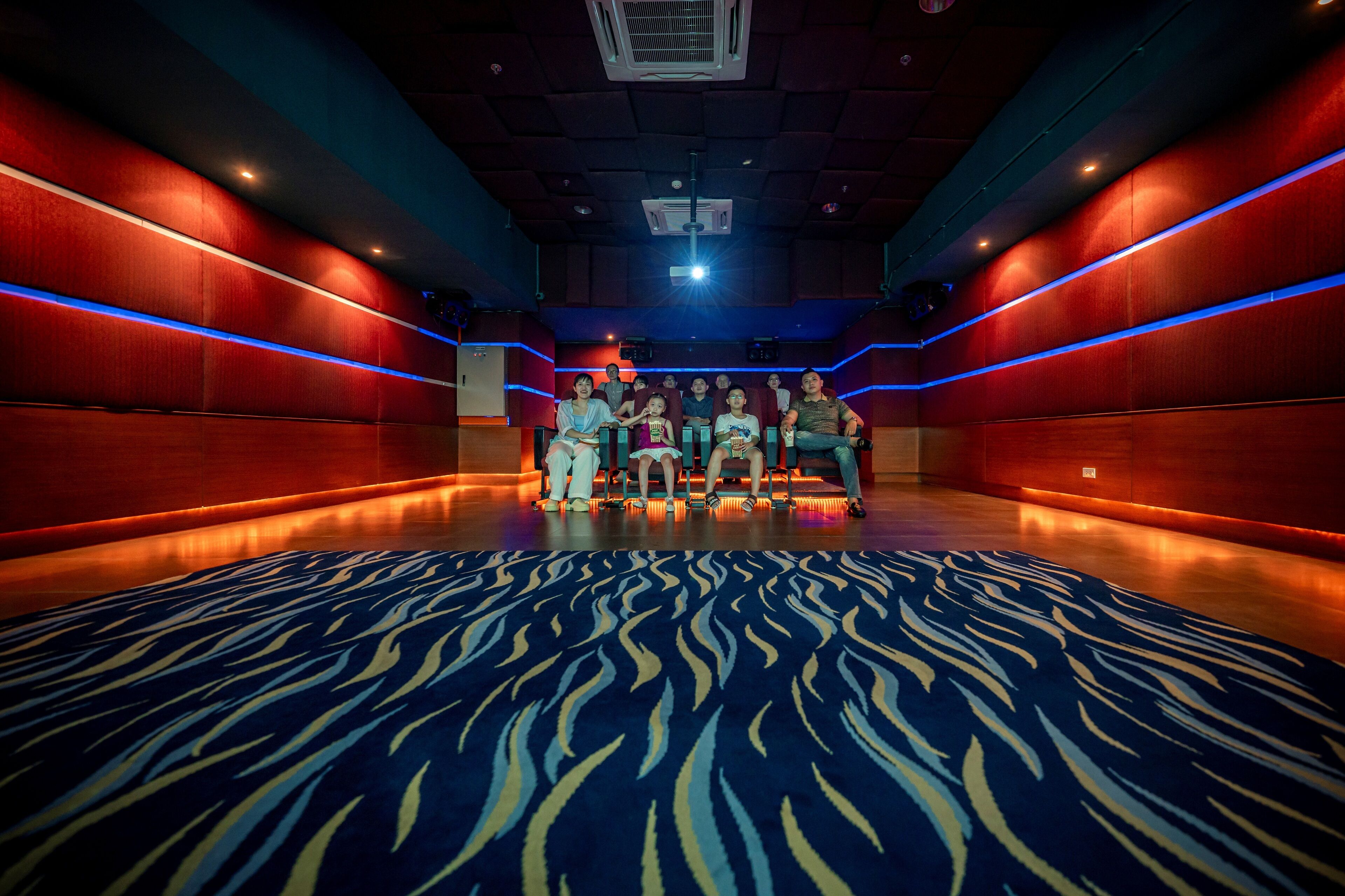 Een theater met een patroonrijk tapijt, rode muren en een groep mensen die op de eerste rij zitten.