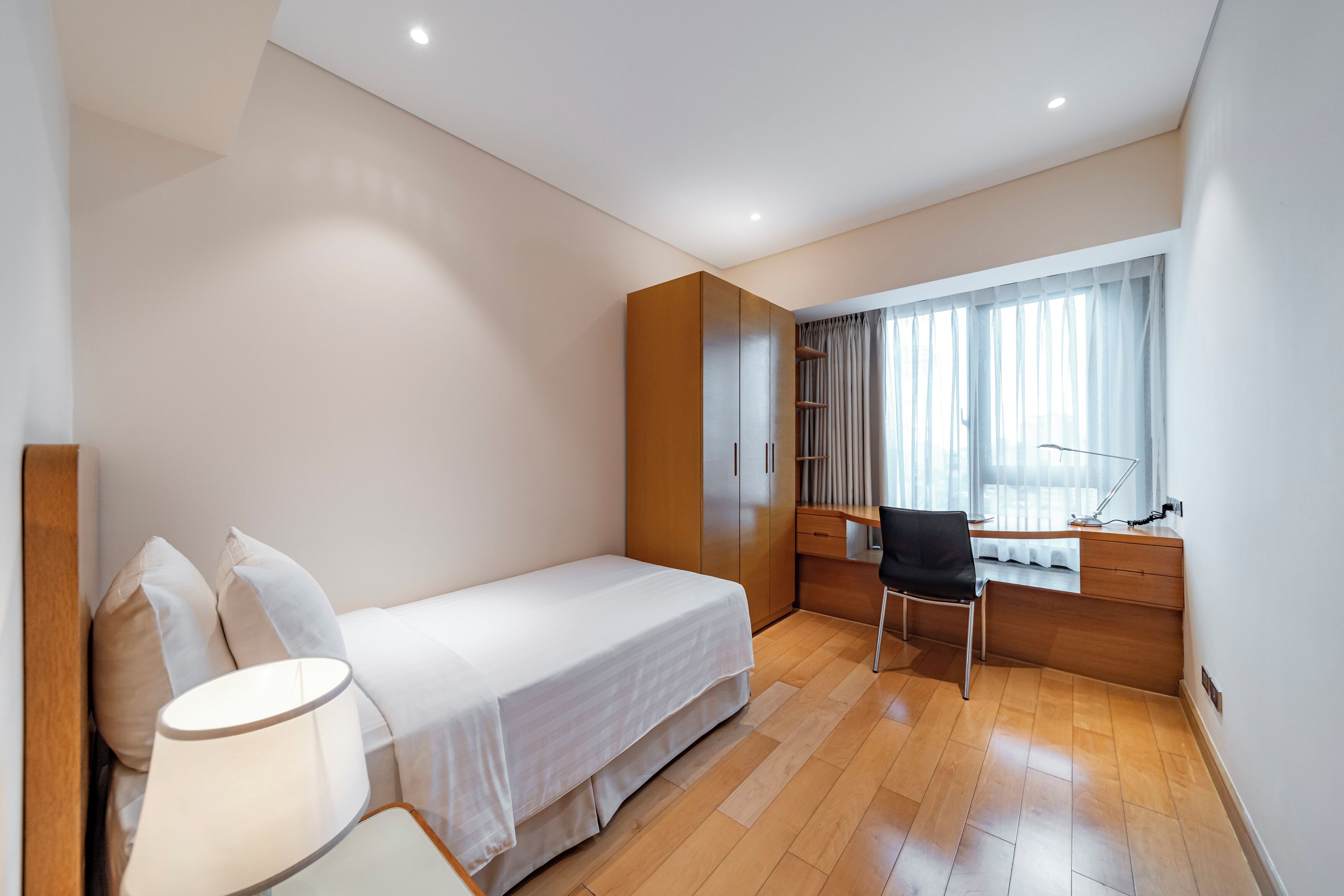 A modern bedroom with a single bed, a desk, a chair, and a large window with curtains.
