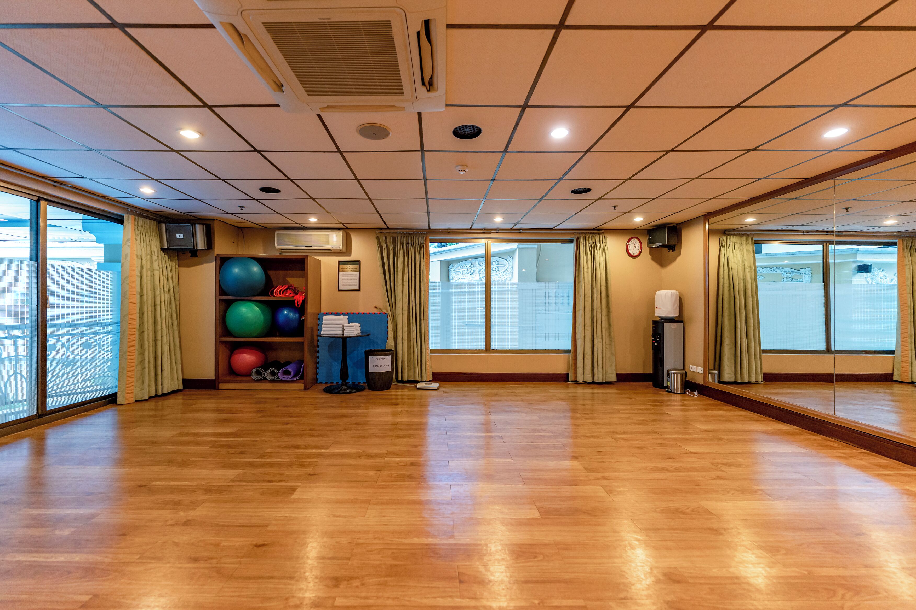A spacious room with wooden flooring, large windows with curtains, exercise balls, and a mirror.