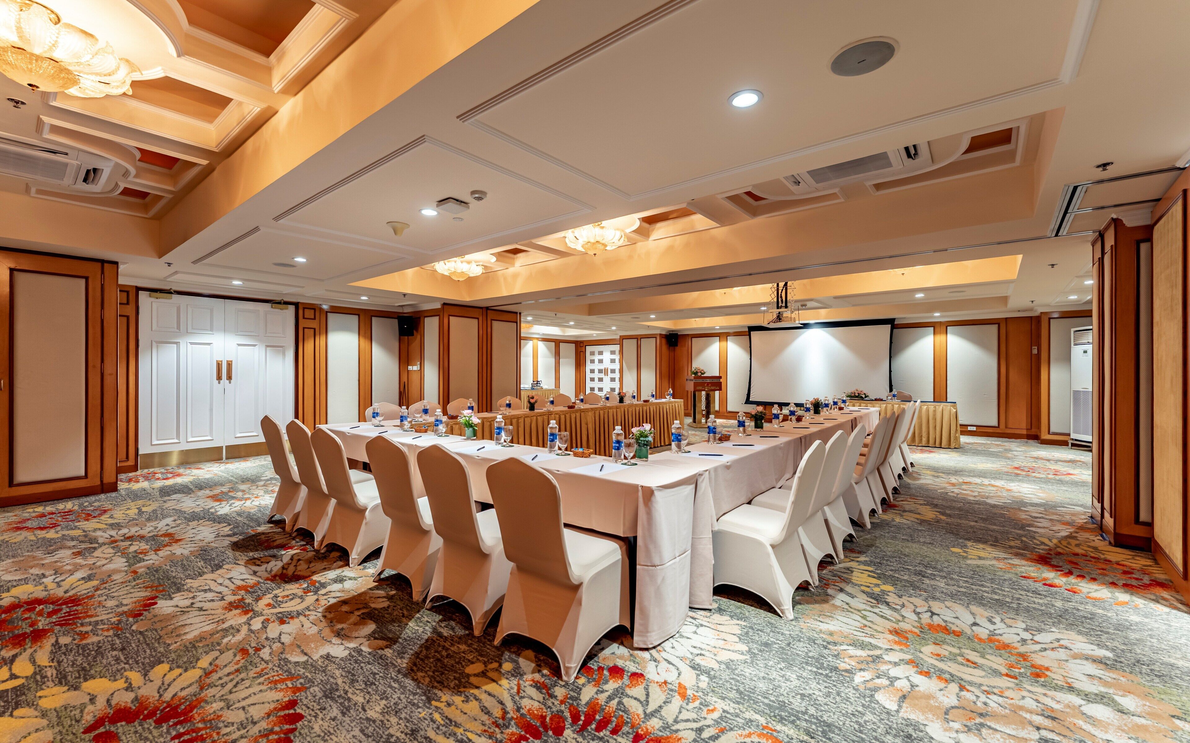 A conference room with a long table, chairs, a projector screen, and a carpeted floor.