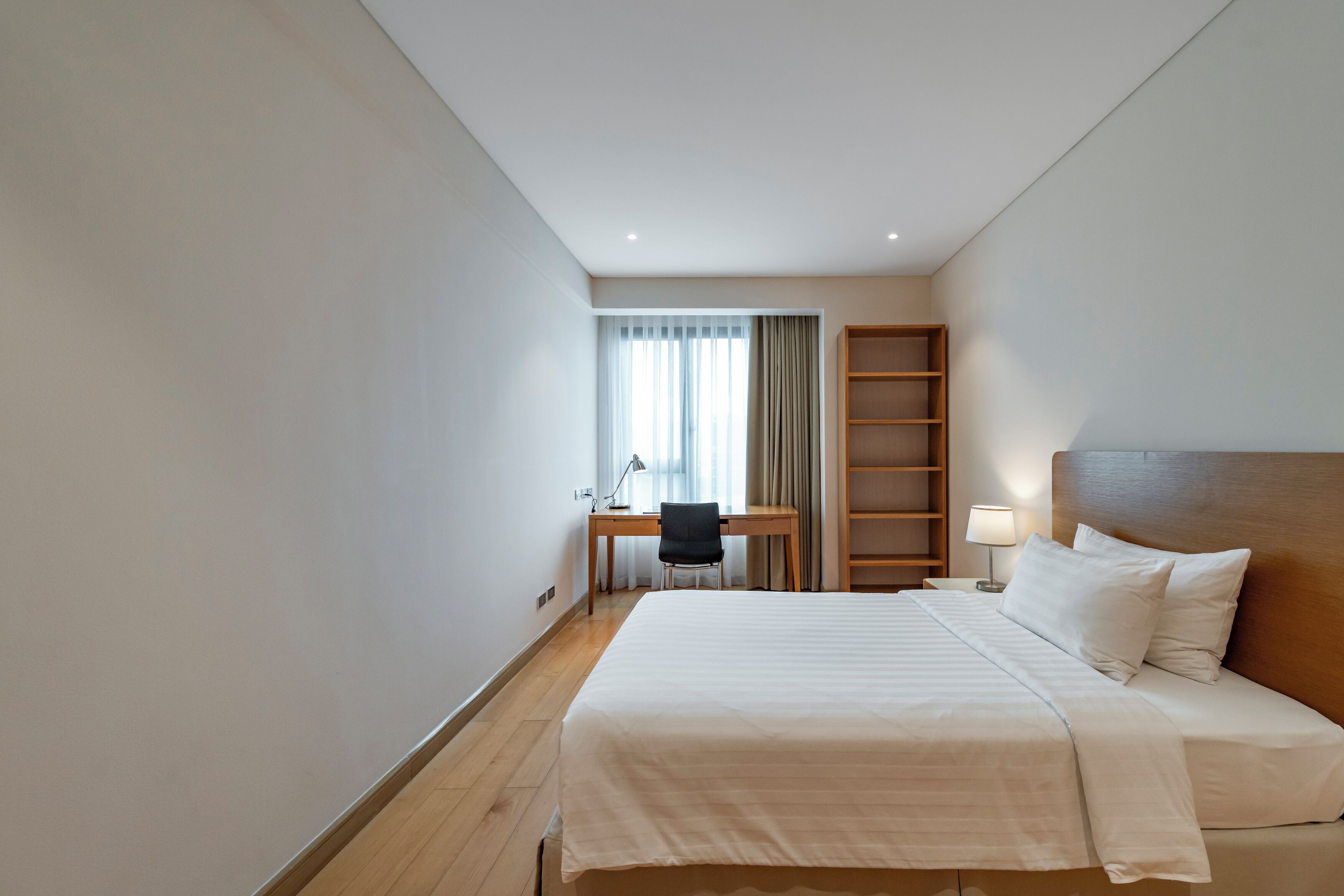 Una habitación de hotel con una cama grande, un escritorio con silla, una mesita de noche y una estantería.