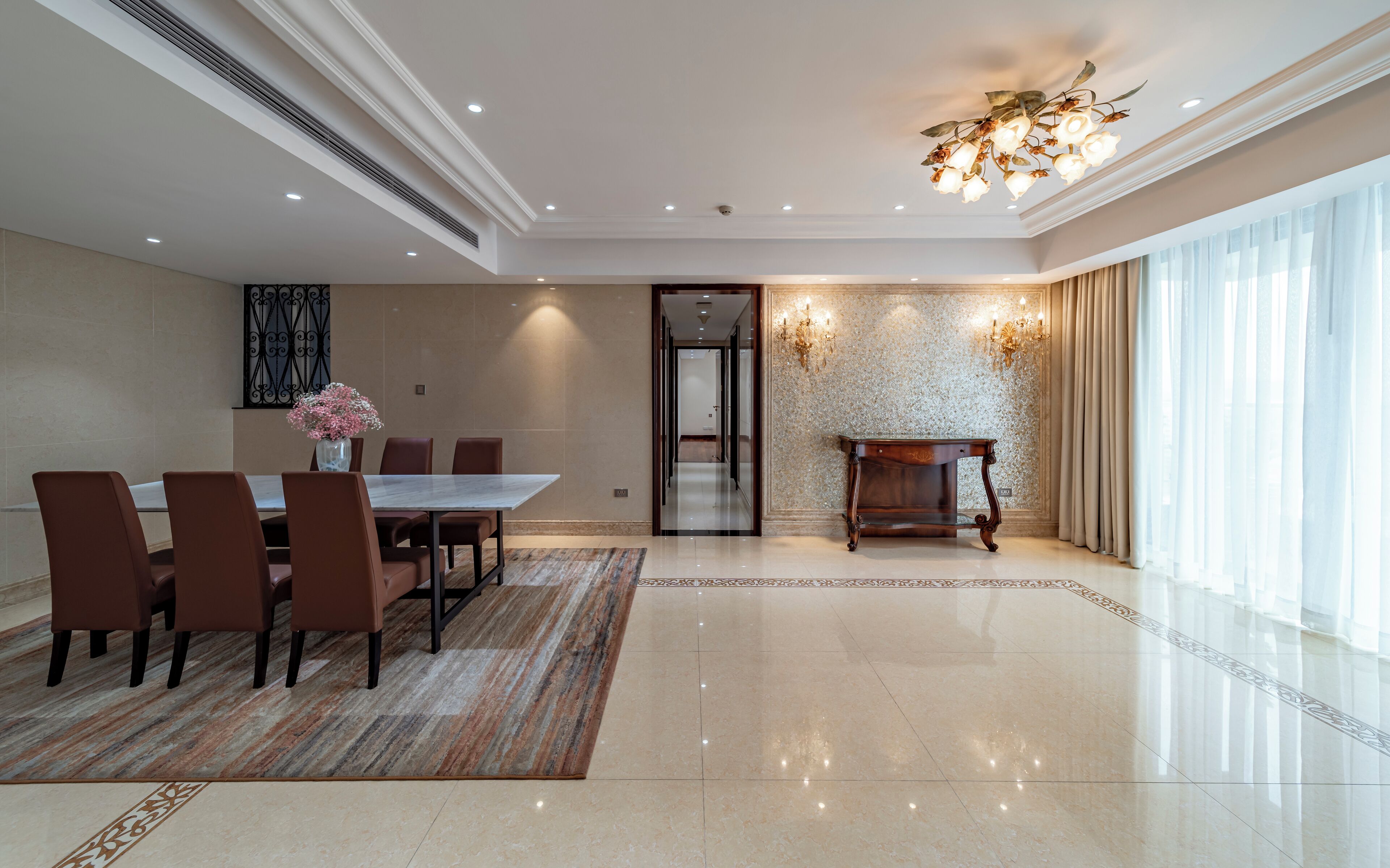 A spacious room with a large dining table, chairs, a chandelier, and a view of the outdoors.