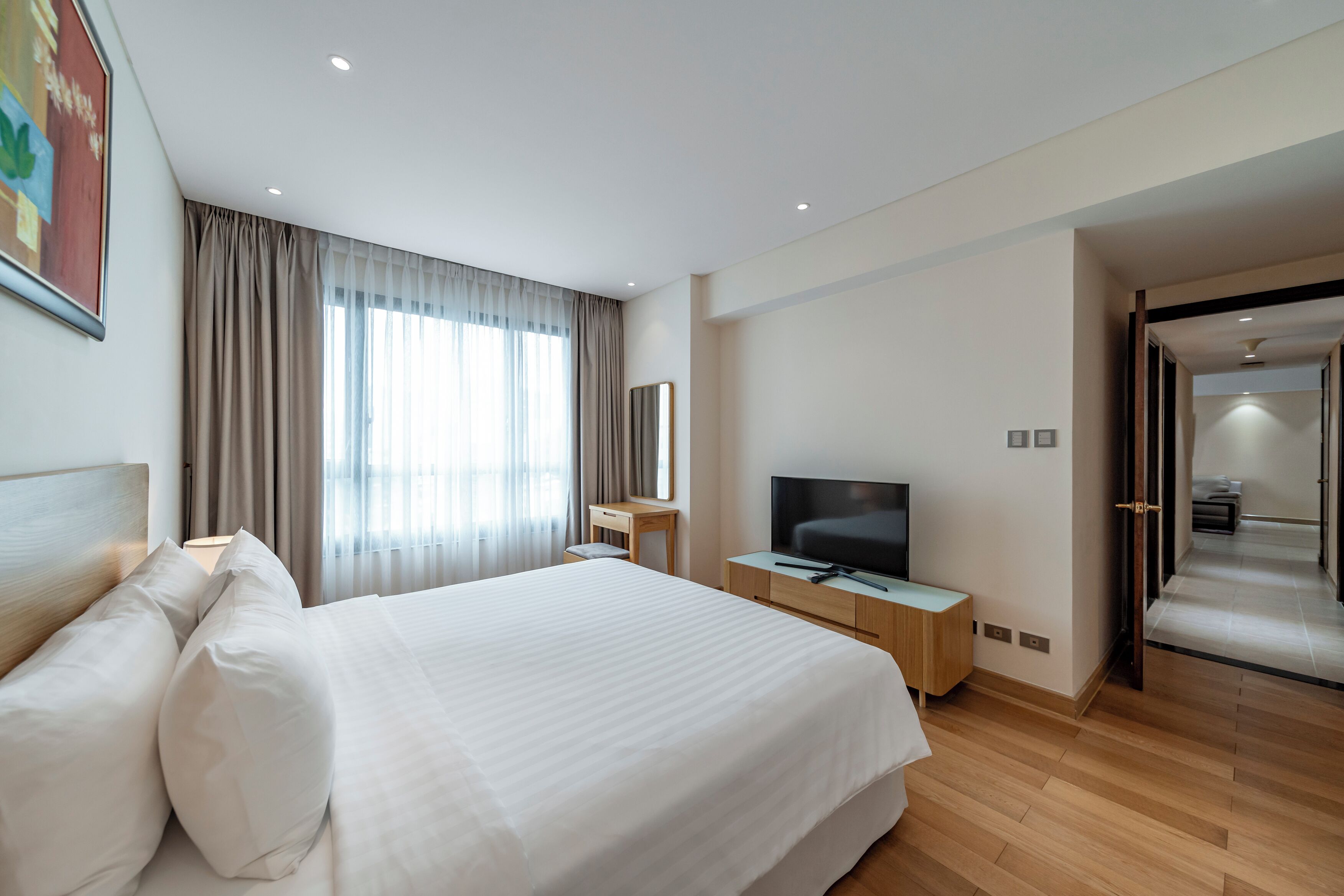 A hotel room with a large bed, a TV, a desk, and a window with curtains.