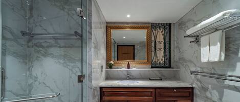 Un baño con pared de mármol, tocador de madera, cabina de ducha de vidrio y un espejo grande con marco dorado.