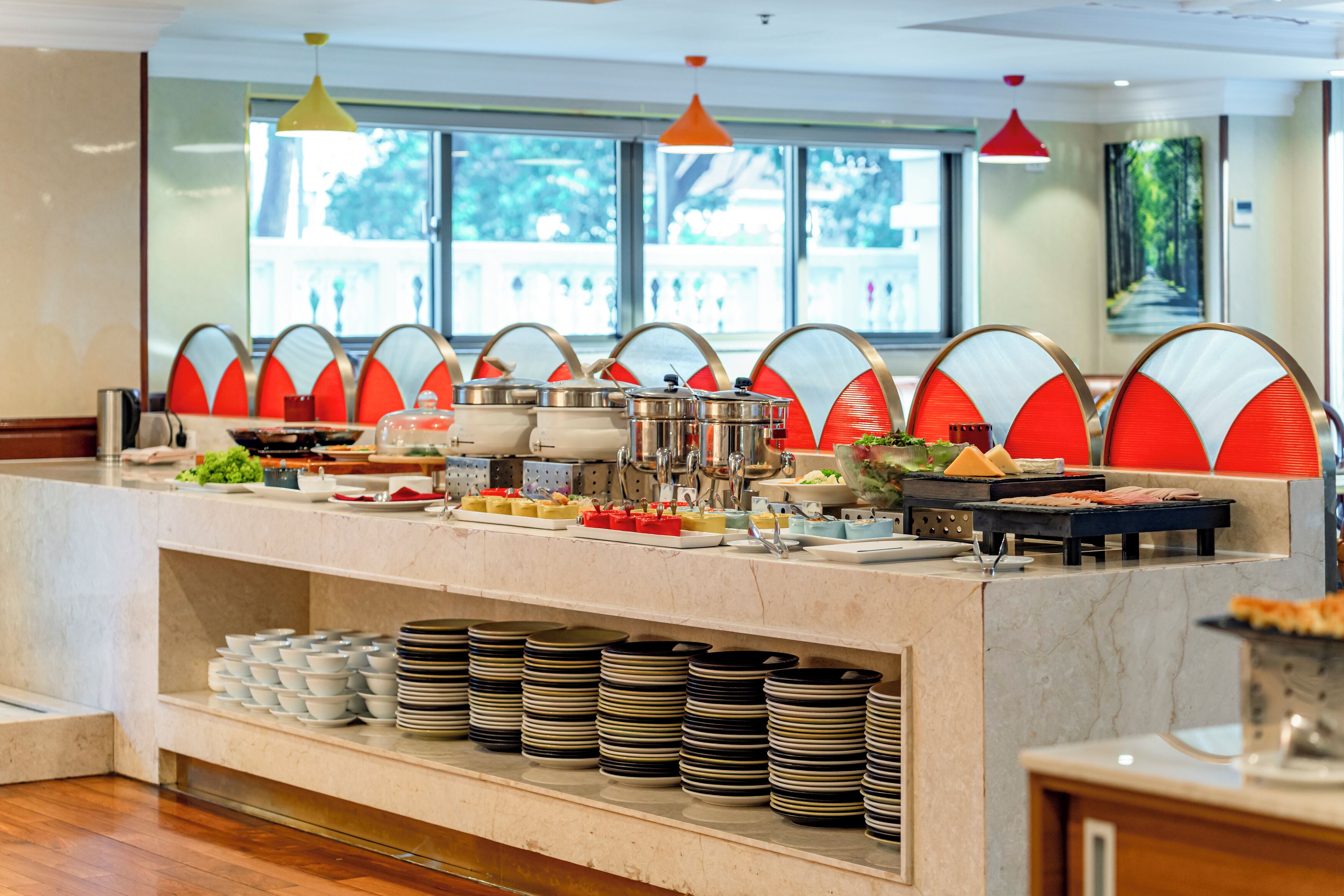 A buffet setup with various food items and utensils, arranged on a marble counter with a view of the outdoors through large windows.
