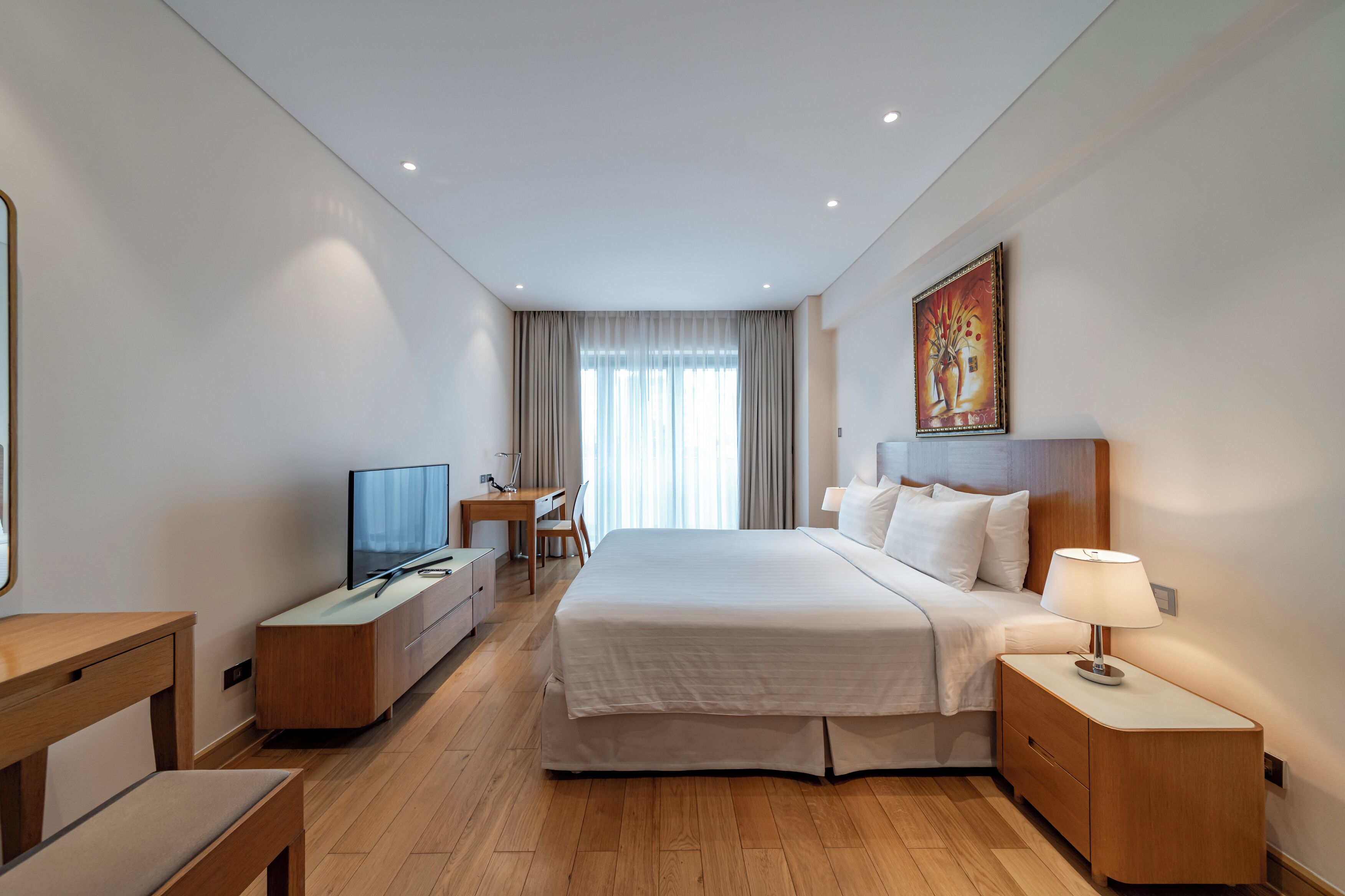 A modern hotel room with a large bed, bedside table, desk, and television.