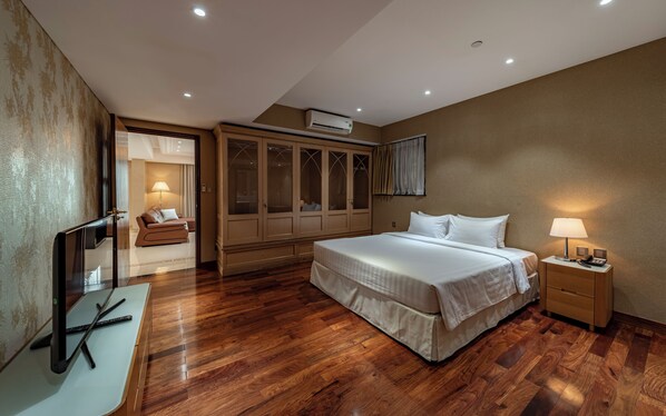 A modern bedroom with a large bed, a wardrobe, a desk with a computer, and a bedside lamp.
