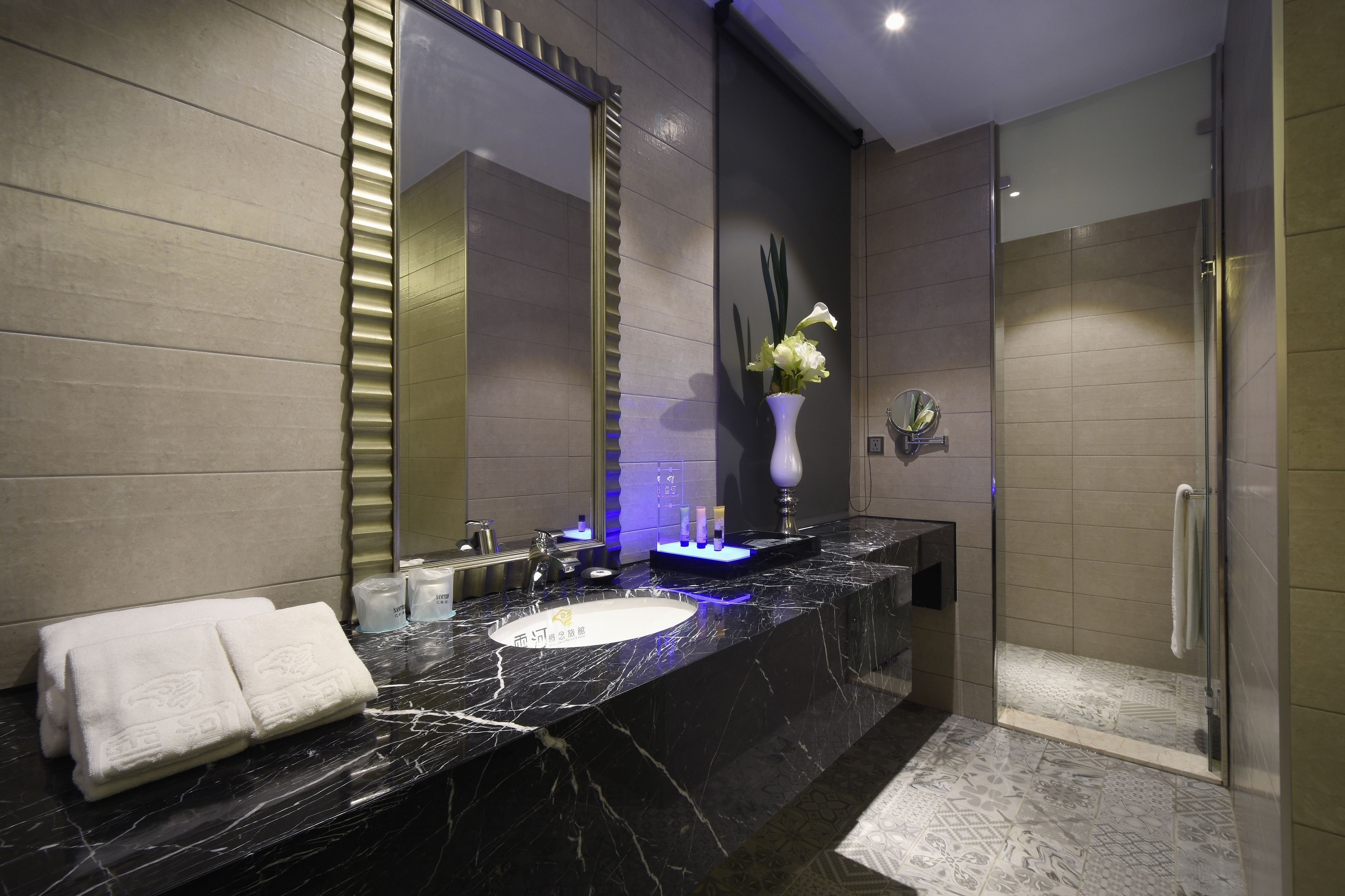 A modern bathroom with a marble sink, a large mirror, and a glass shower enclosure.
