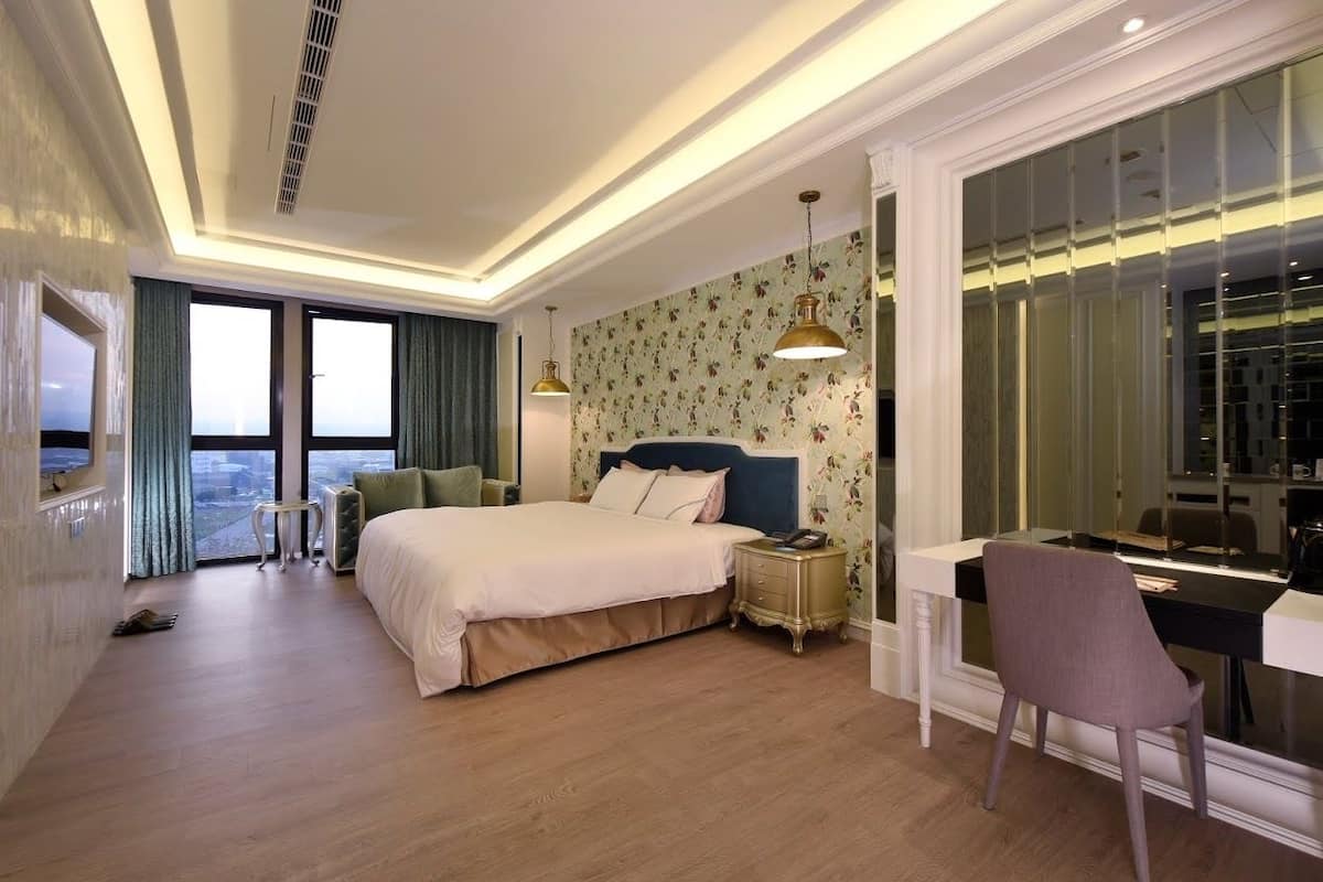 Hotelkamer met een groot bed, een bureau en een stoel. Er is uitzicht op de stad door de ramen.