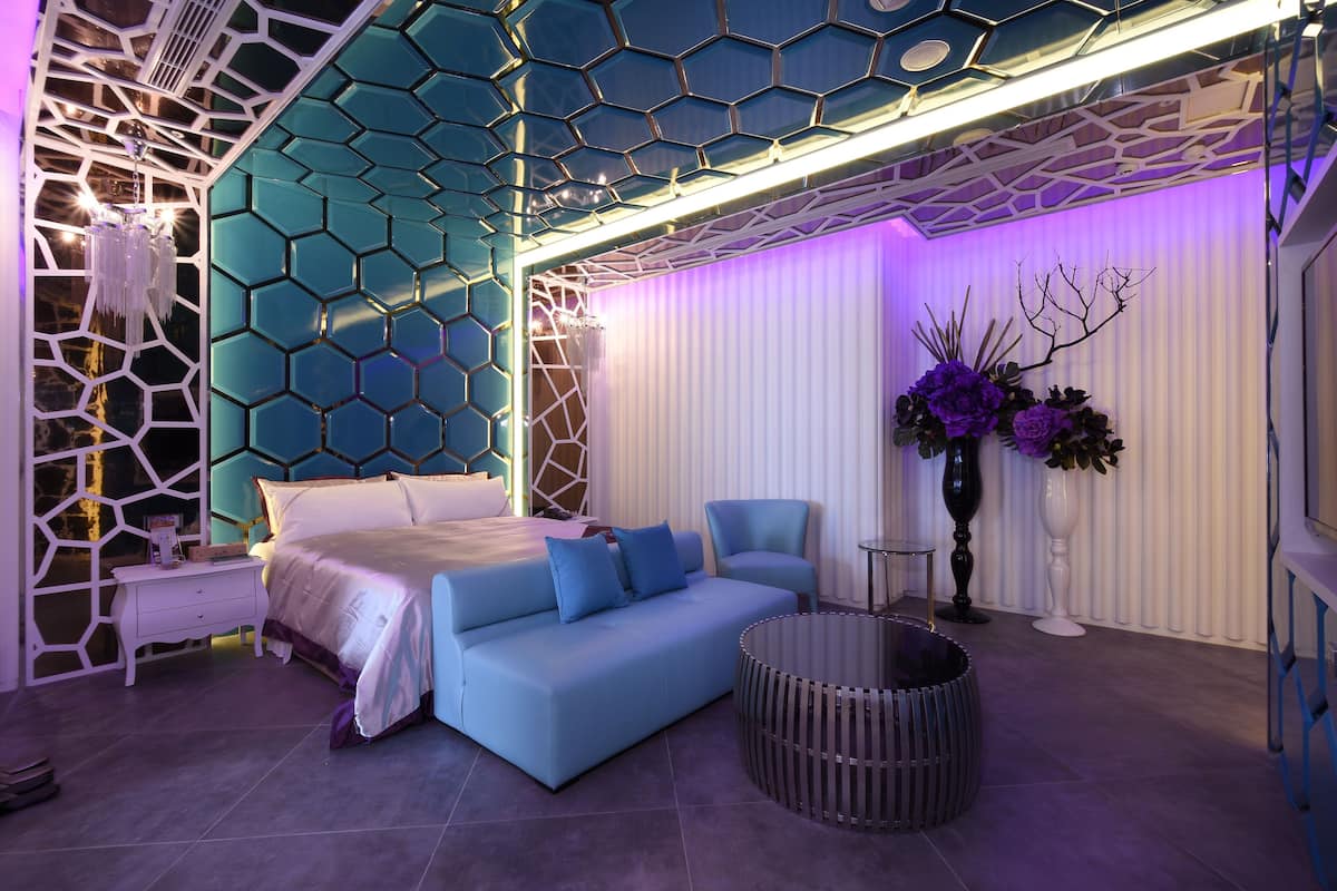 Een moderne slaapkamer met een blauwe bank, een bed, een nachtkastje, een rond bijzettafeltje en een decoratieve vaas met bloemen.