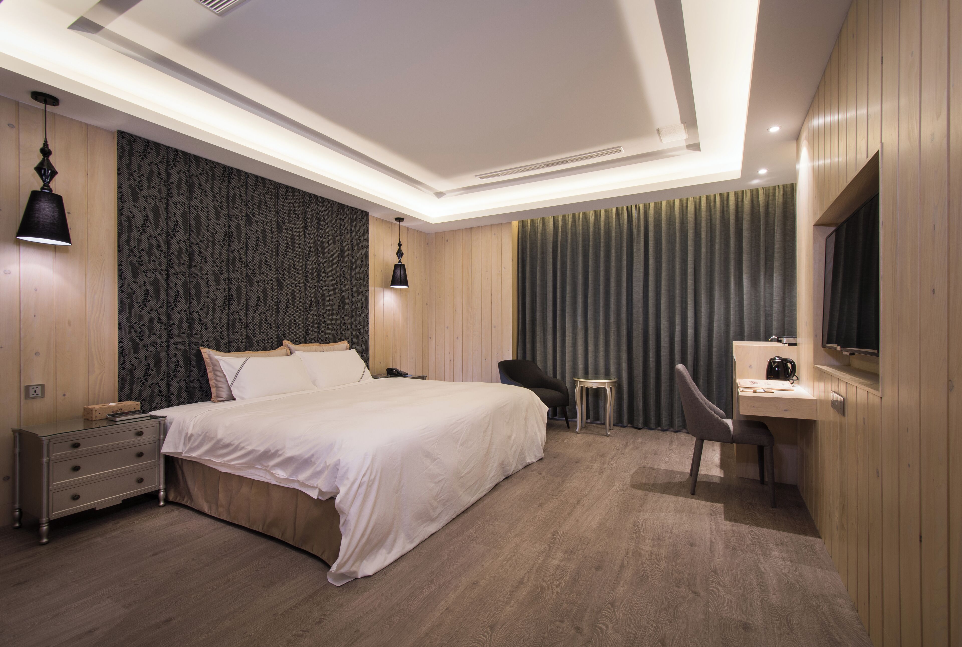 A modern hotel room with a large bed, a desk, a chair, and a TV.