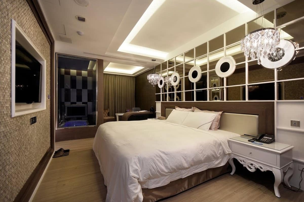 Een moderne hotelkamer met een groot bed, nachtkastje, spiegel en een kroonluchter.