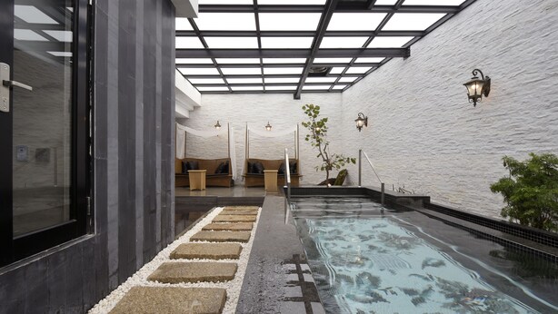 Een wellnessruimte met een glazen zwembad, zitplaatsen aan het zwembad en een wit, gestructureerd muur.