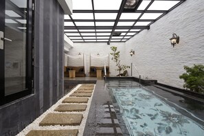 Un espace spa doté d’une piscine à laquelle on accède par une paroi de verre, de sièges installés au bord de la piscine et d’un mur blanc à la texture particulière.