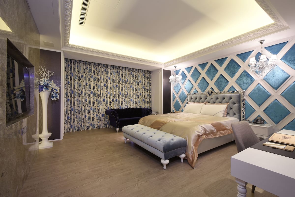 Een slaapkamer met een groot bed, een bankje, een kaptafel en een dressoir.