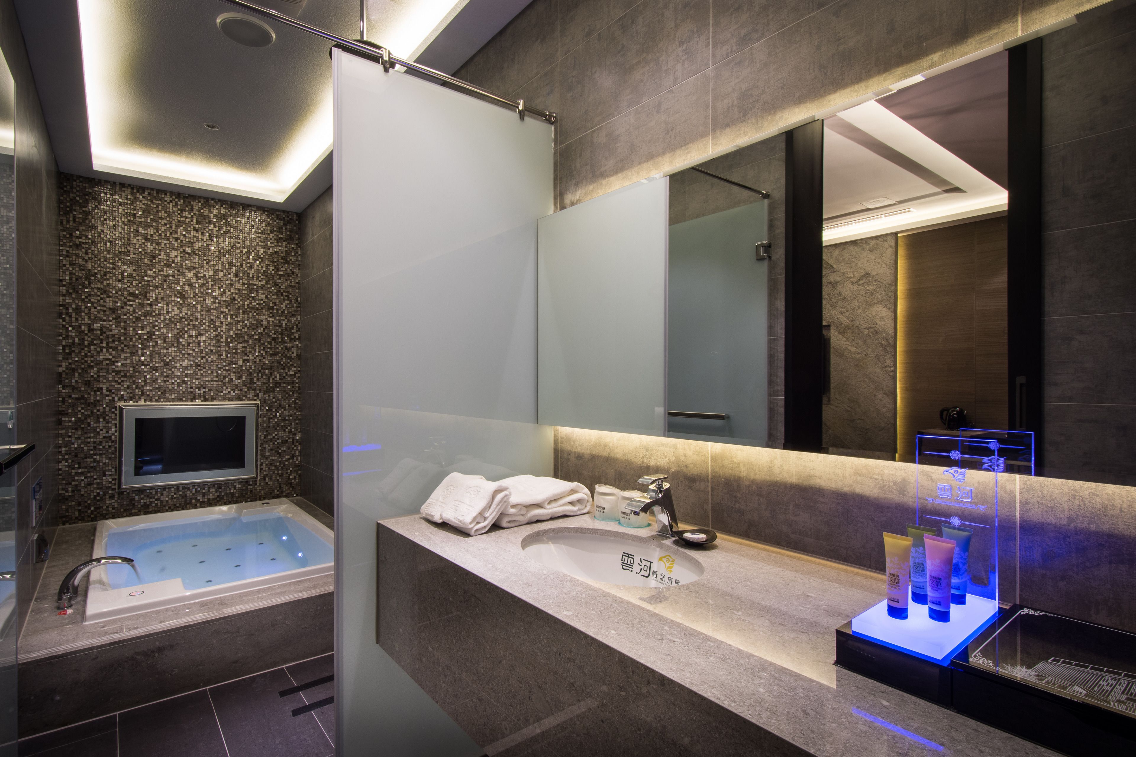 A modern bathroom with a glass-enclosed shower, a large mirror, and a vanity with a sink and toiletries.