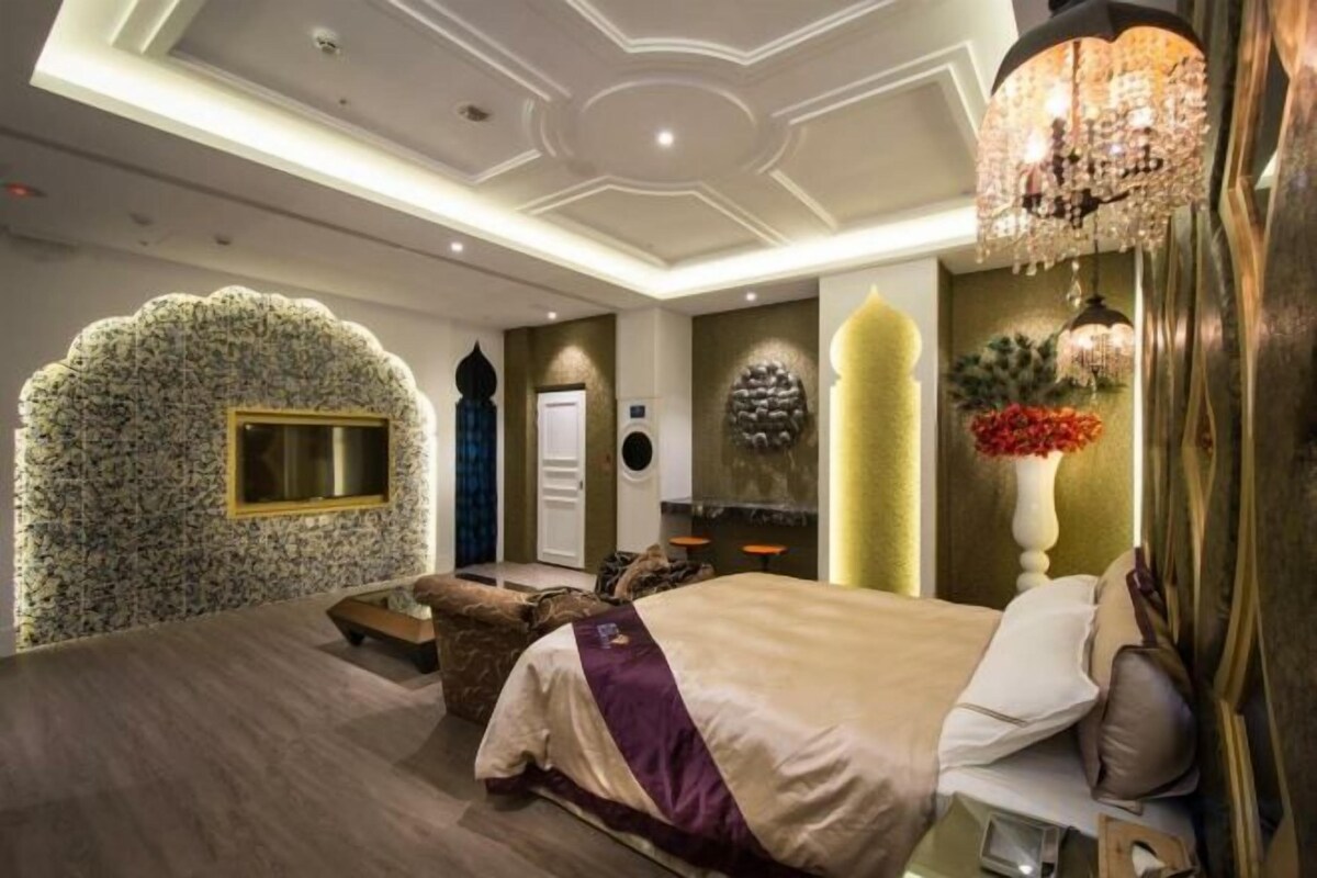 A bedroom with a large bed, a seating area, a wall-mounted TV, and a decorative wall.