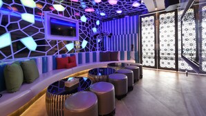 Een moderne lounge met een gebogen zithoek, een decoratieve muur met geometrische patronen, en een groot raam met een patroonrijk uitzicht.