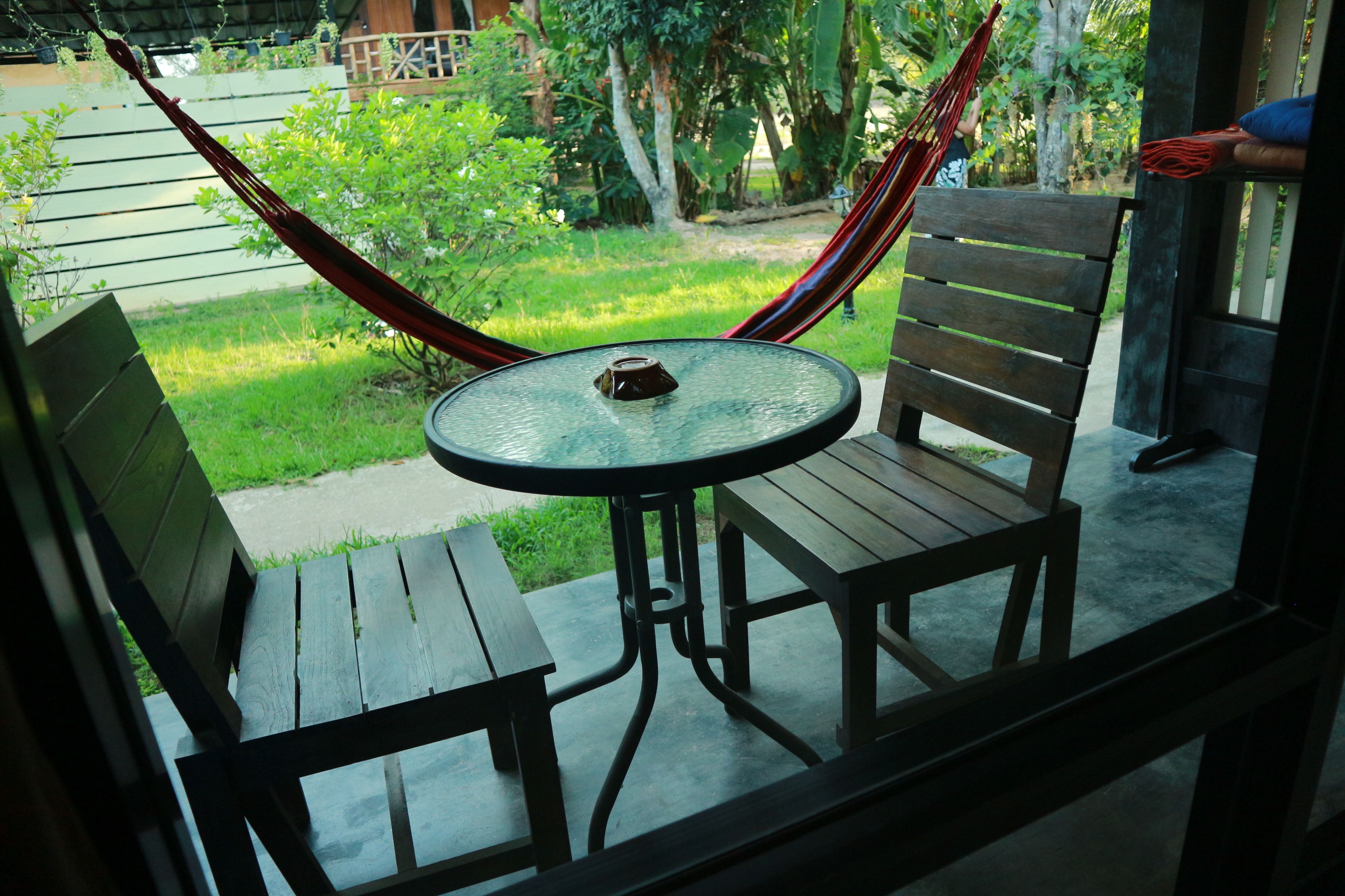 Een houten bank en tafel op een veranda, met uitzicht op een tuin en een hangmat.