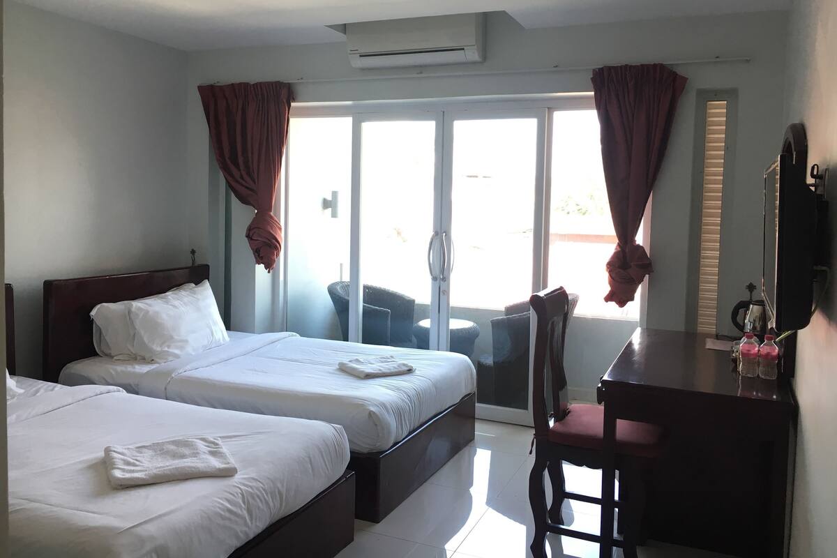 Una habitación de hotel con dos camas, un escritorio, una silla y un ventanal con cortinas.