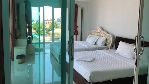Une chambre d’hôtel avec deux lits, un balcon donnant sur des immeubles et une porte vitrée menant à un espace balcon.