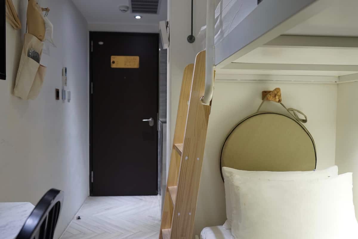 A hotel room with a bed, a wooden ladder, a door, and a small shelf with a bottle.