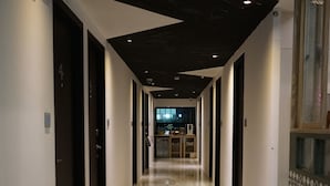 Um corredor com chão de mármore polido, teto de madeira escura e vista para um quarto com escrivaninha e cadeira.