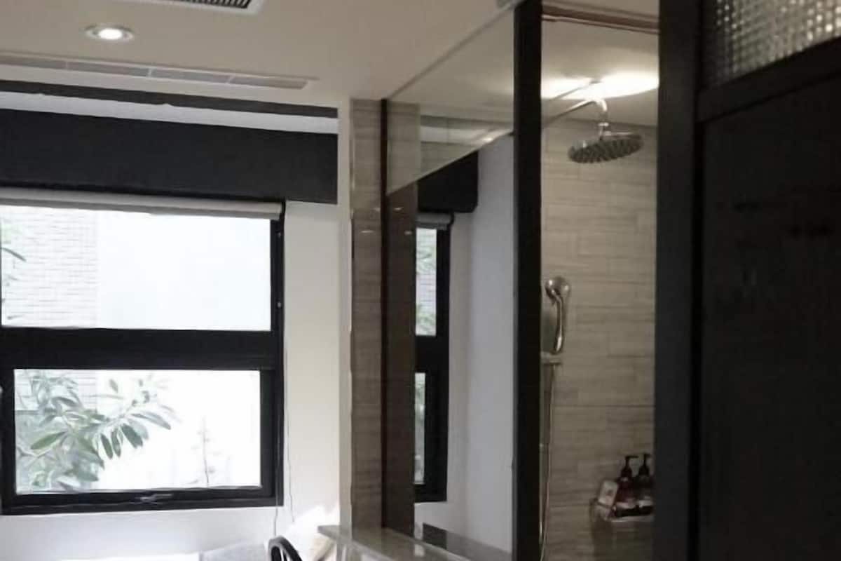 A modern hotel room with a bed, a chair, a shower area, and a window with a view.