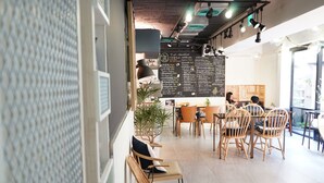 Um café com cadeiras de vime, um quadro negro com o menu e uma mesa de madeira.