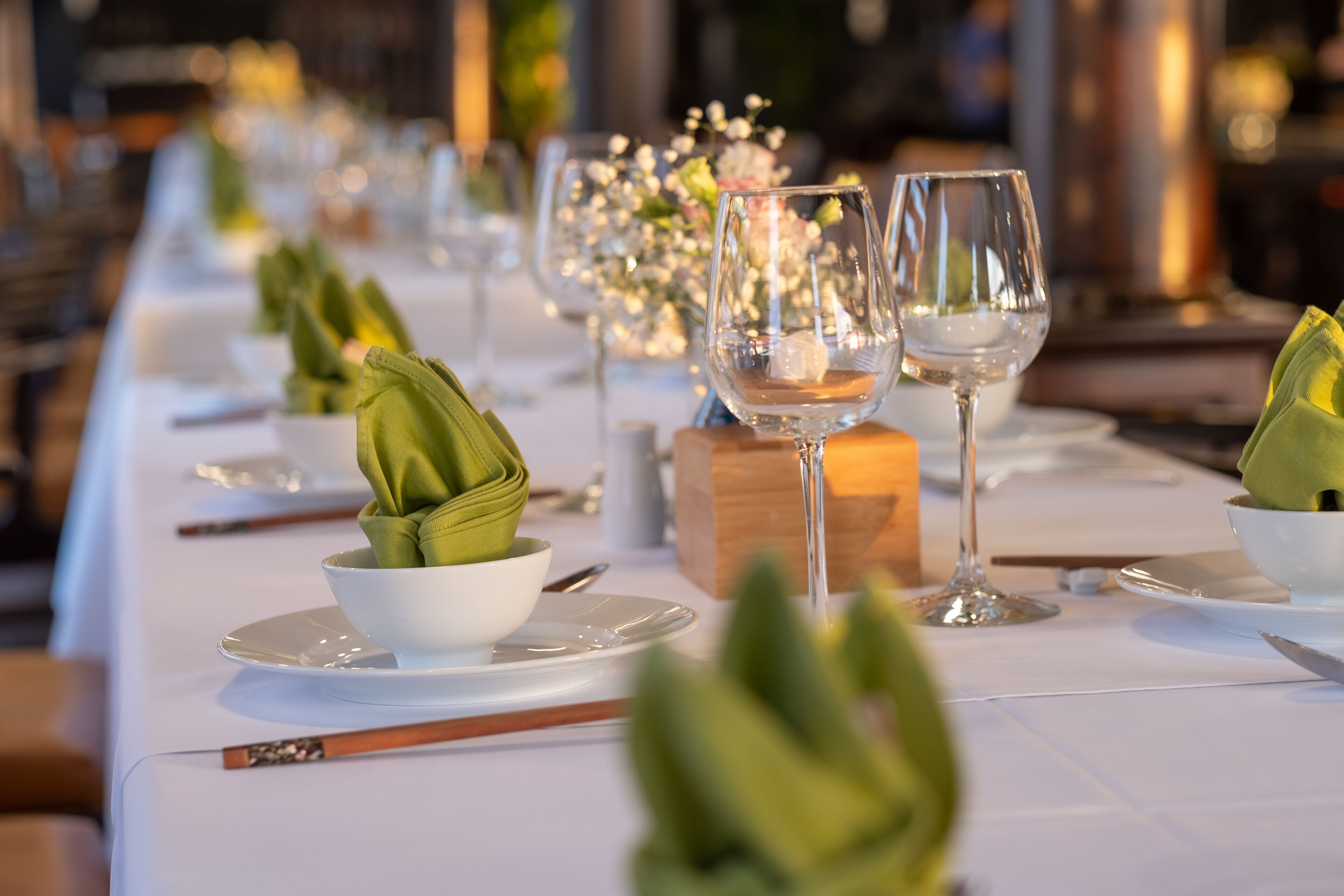 A long dining table set with white plates, bowls, and green napkins.