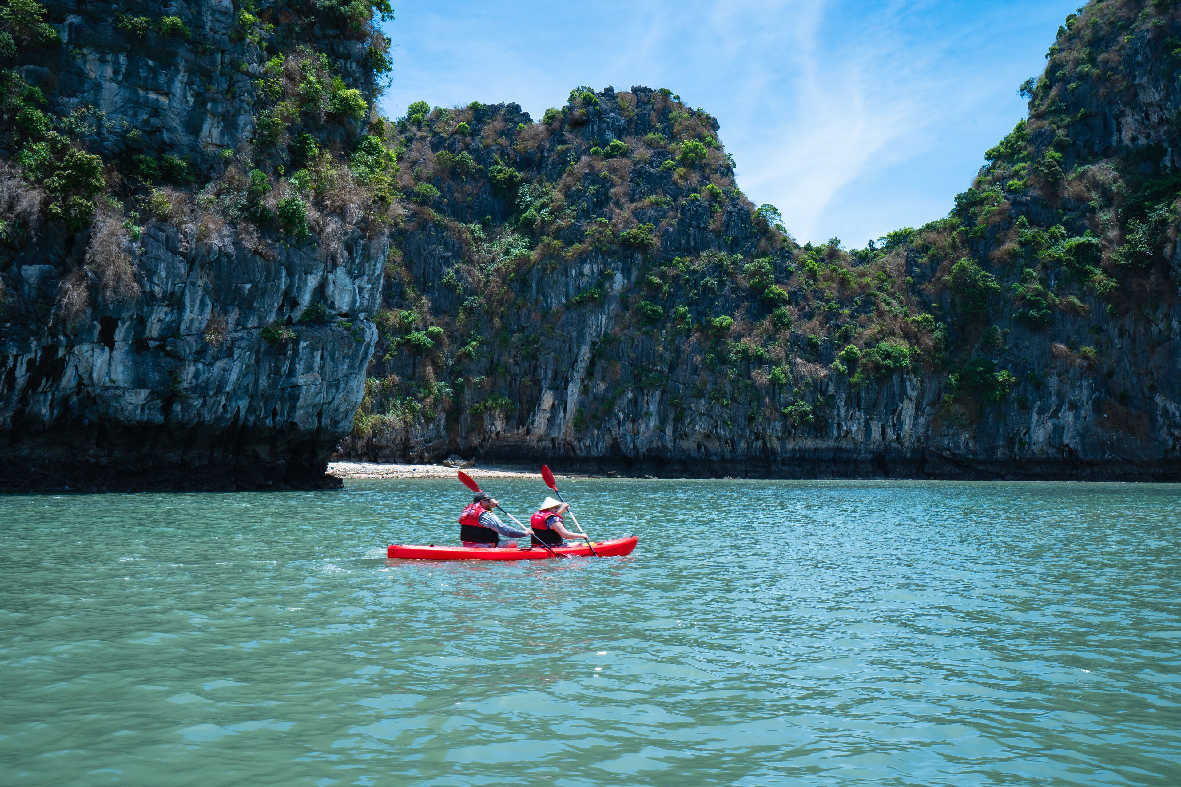 A kayaker in a red kayak on calm water with a rocky cliff in the background.
