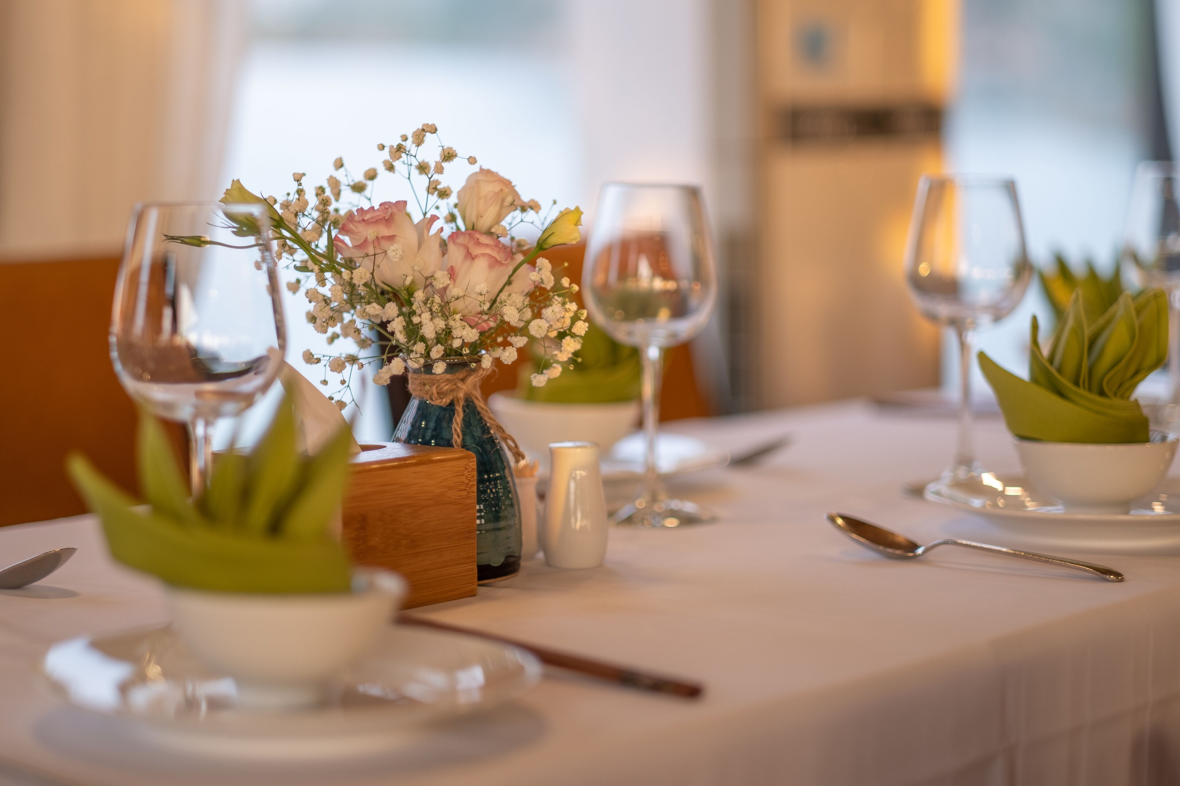 A dining table set with wine glasses, bowls, and a centerpiece of flowers.