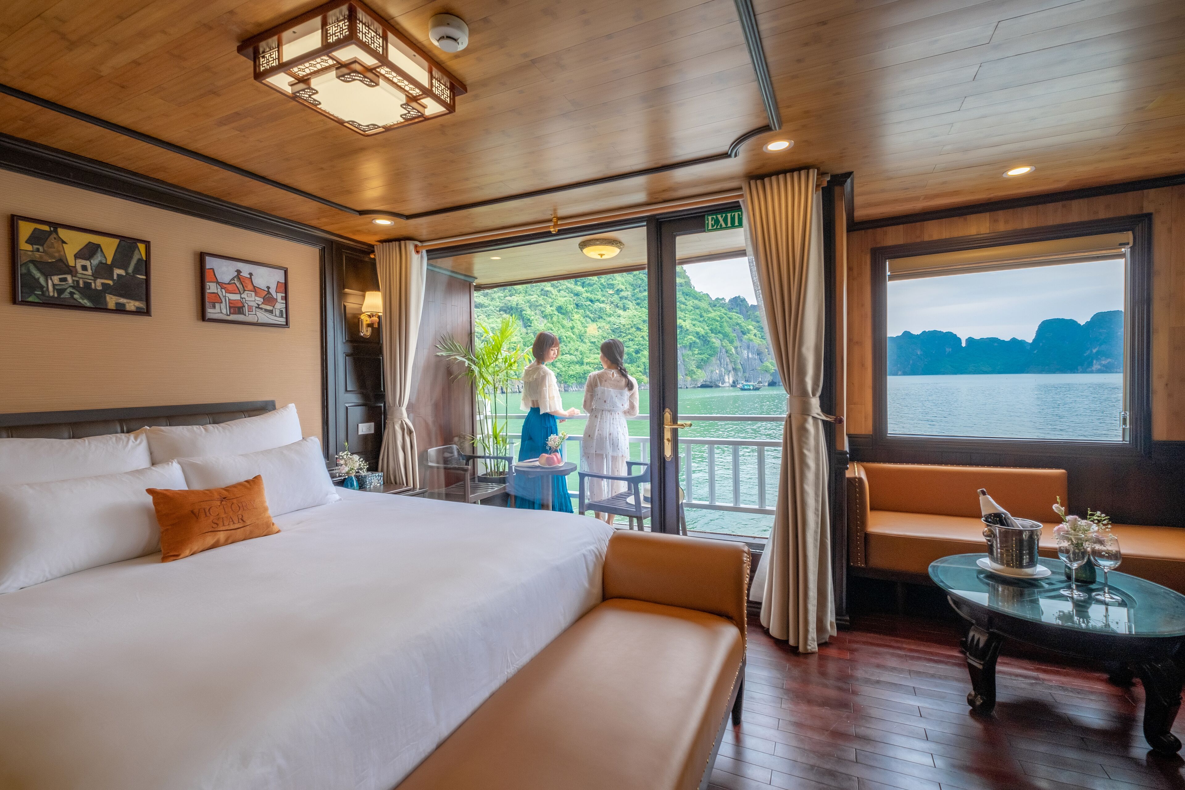 A hotel room with a large bed, a balcony with a view of the water, and a seating area with a table.
