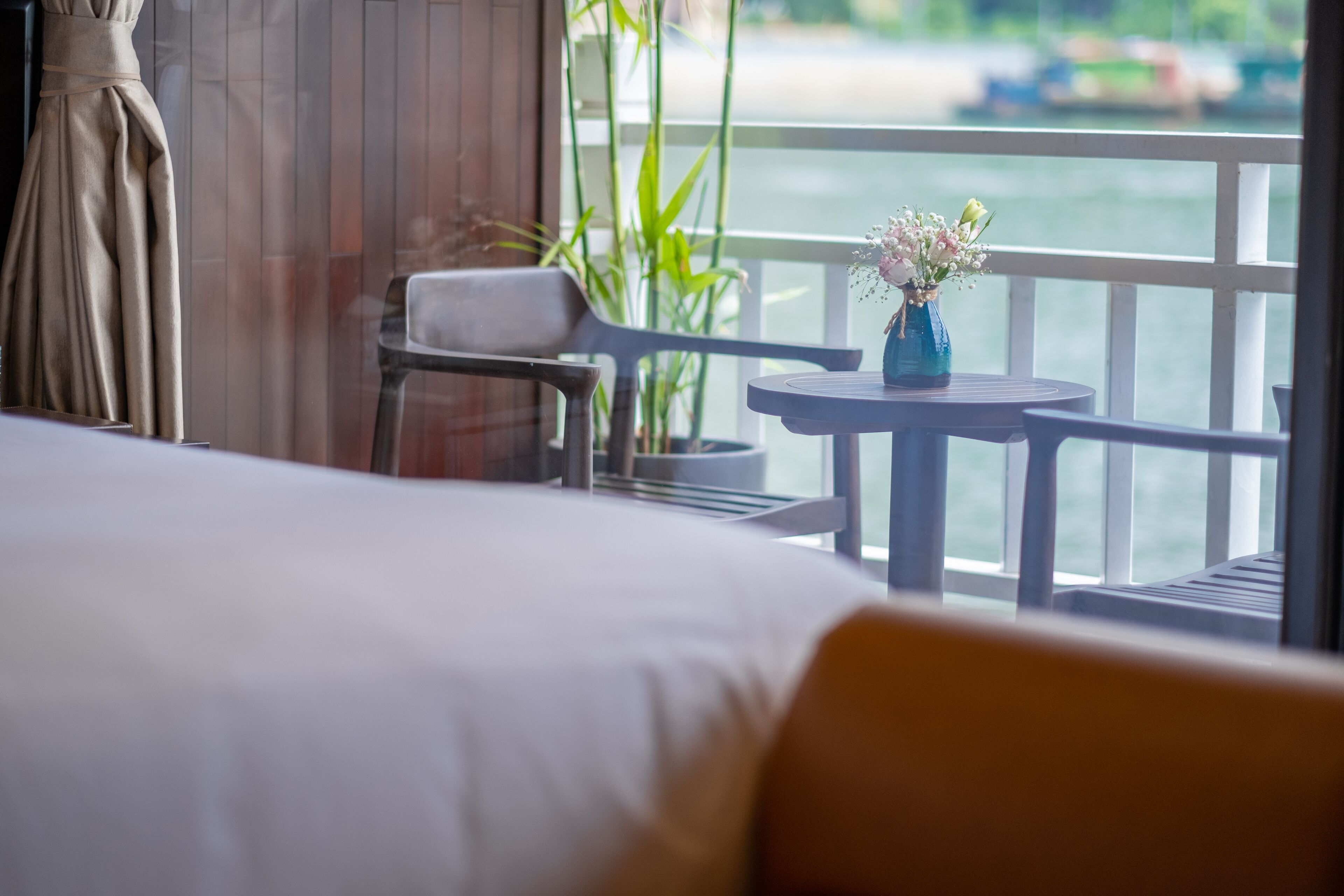 Une chambre d’hôtel avec un lit, une chaise, une petite table ornée d’un vase de fleurs et une vue sur l’eau.