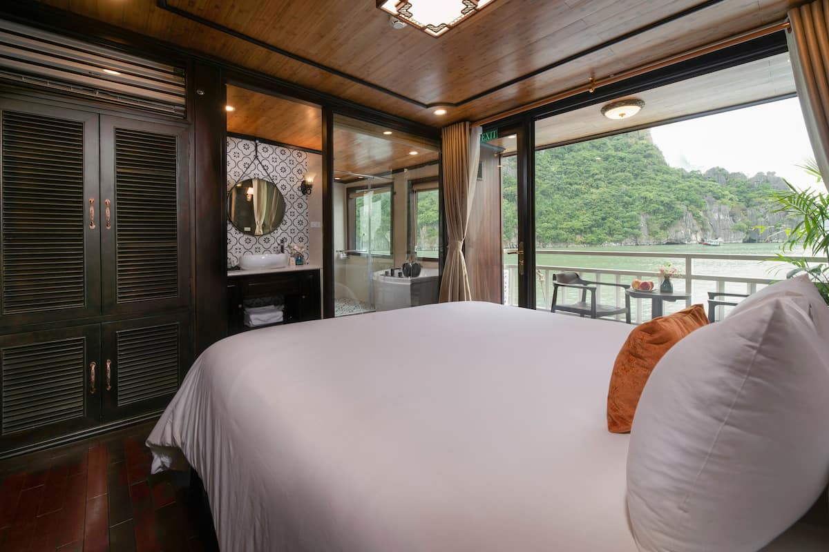 A bedroom with a large bed, a bathroom with a mirror, and a view of a body of water.