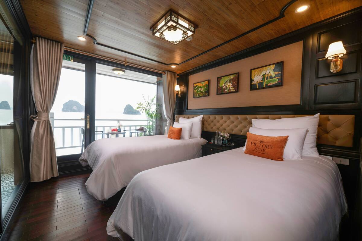 A hotel room with two beds, a wooden ceiling, a balcony with a view, and artwork on the wall.