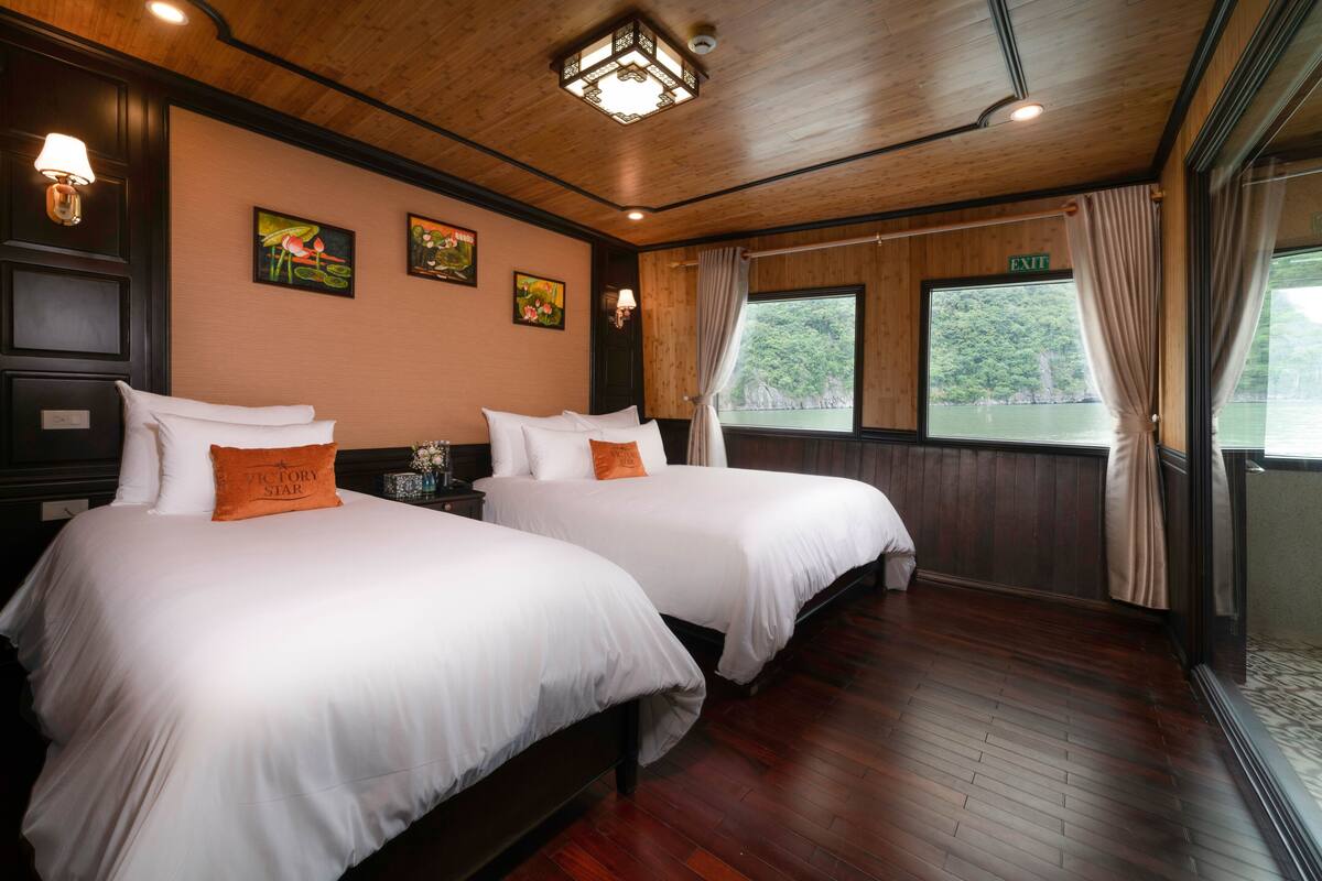 A hotel room with two beds, wooden flooring, and a large window with a view of greenery.