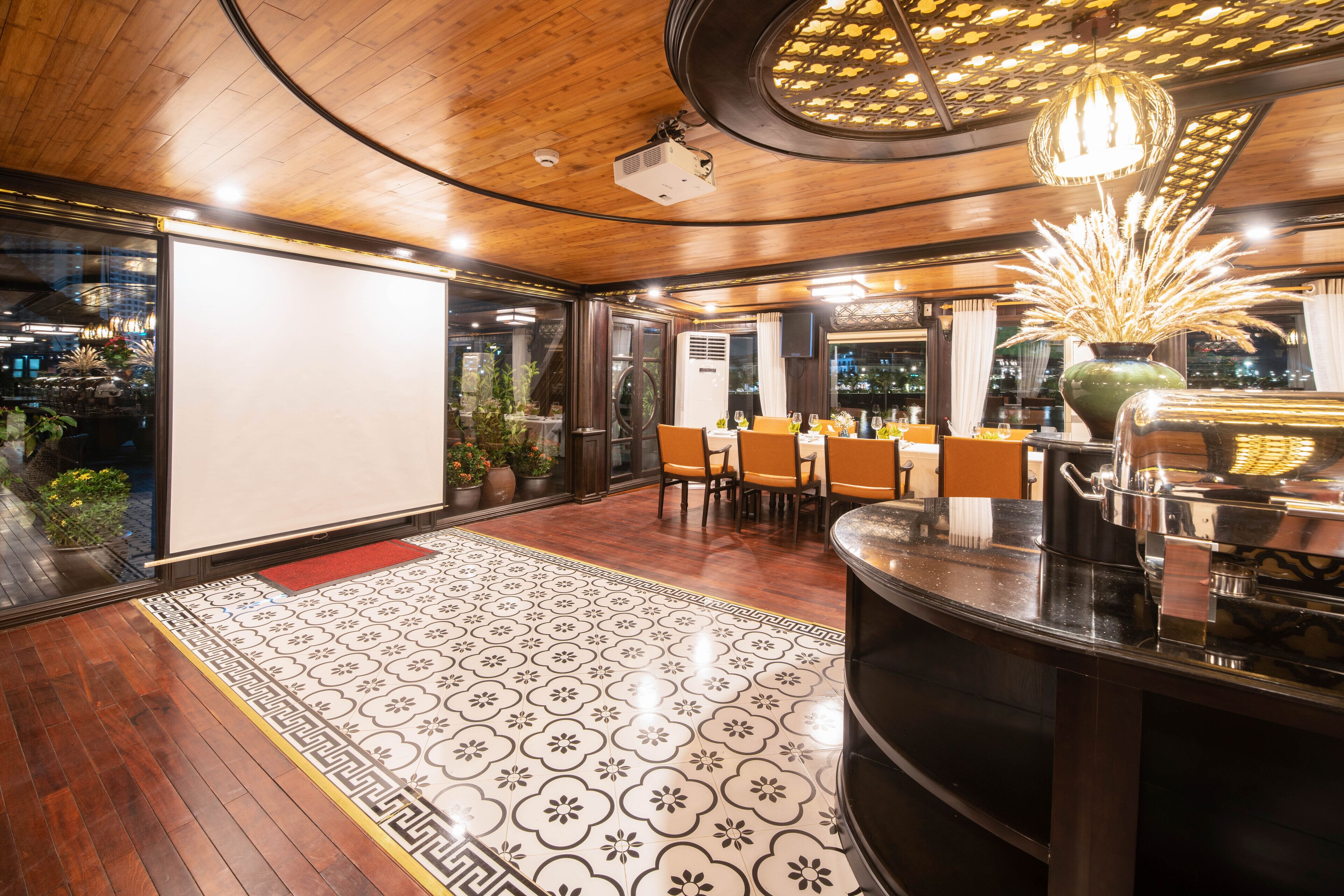 A restaurant with a wooden ceiling, a patterned floor, and a bar area with a large vase of dried plants.