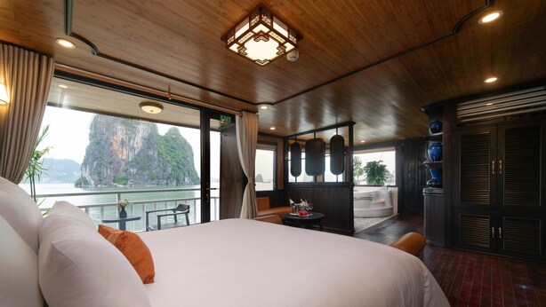 A spacious room with a large bed, a view of a mountainous landscape, and a balcony with a table and chairs.