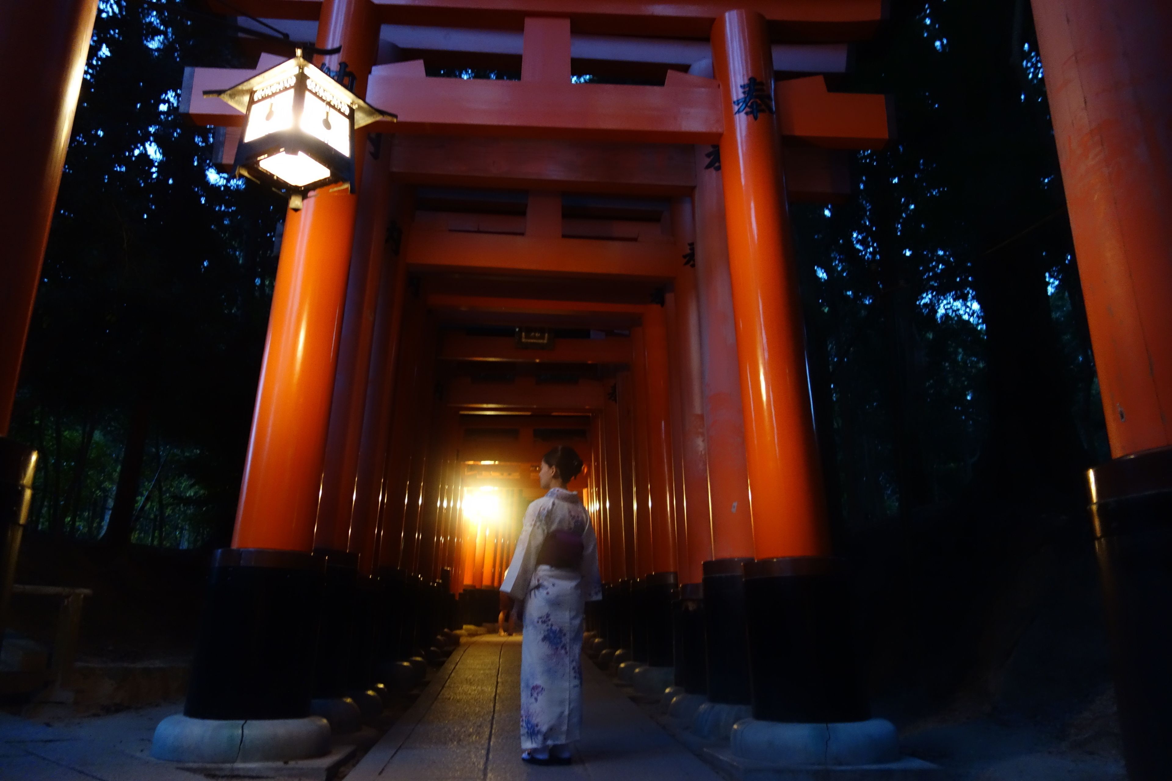 A person walking through a corridor with red pillars and a lit lantern at the end.