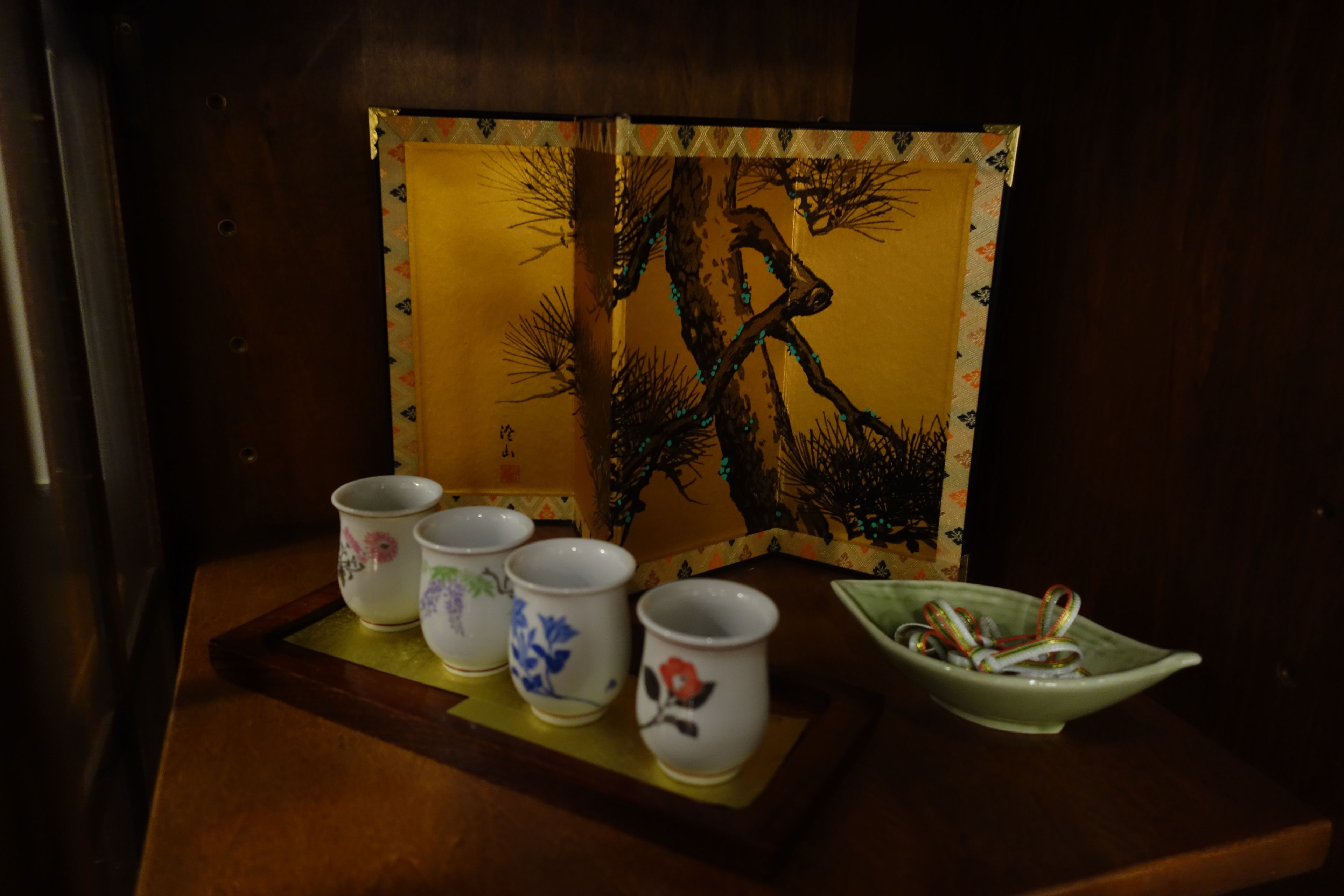 Uma mesa de madeira com quatro chávenas de cerâmica e uma tigela, com um quadro emoldurado ao fundo.