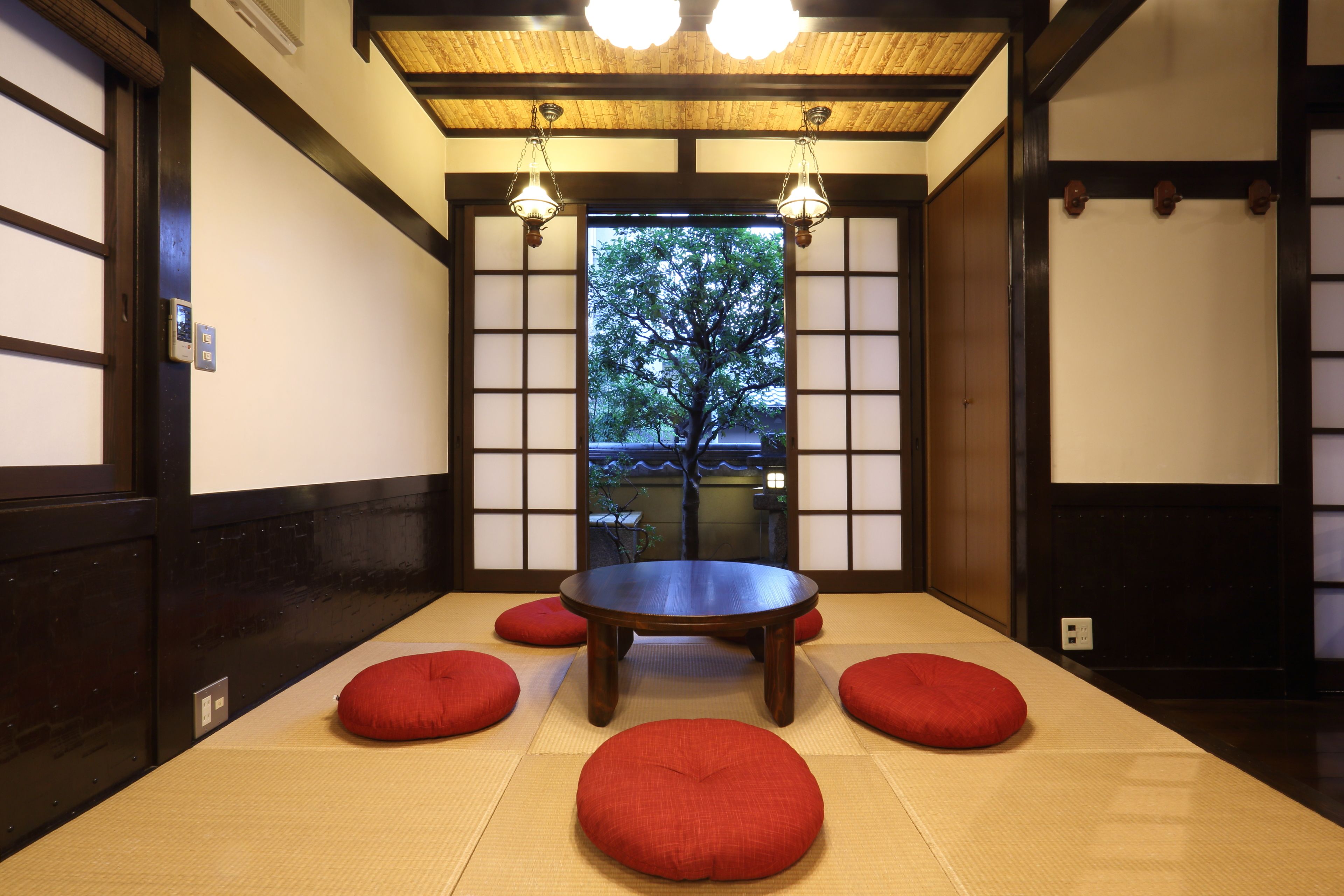 Una habitación tradicional japonesa con suelo de tatami, una mesa de madera baja y cojines rojos.