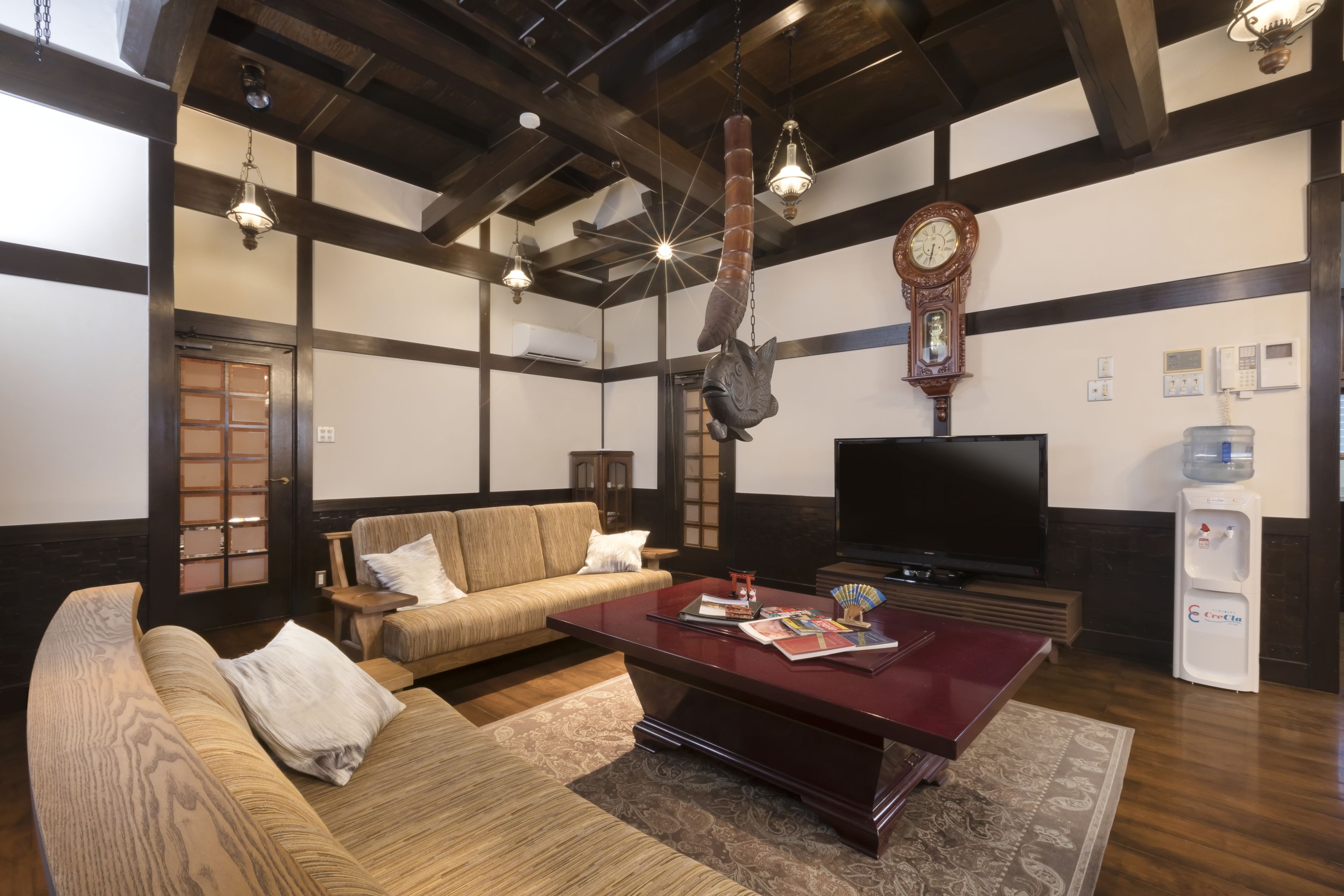 A traditional Japanese-style living room with tatami flooring, a low wooden coffee table, a sofa, and a television.