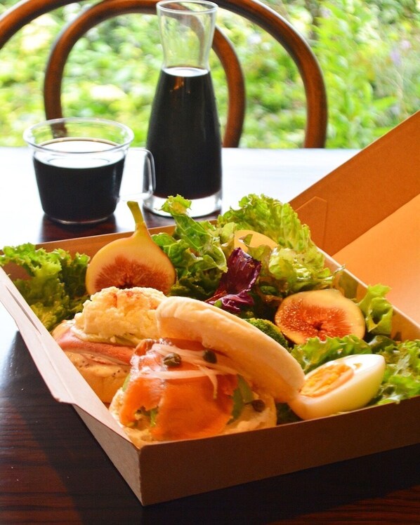 Una comida en una caja de cartón que incluye una ensalada, un sándwich y un huevo cocido.