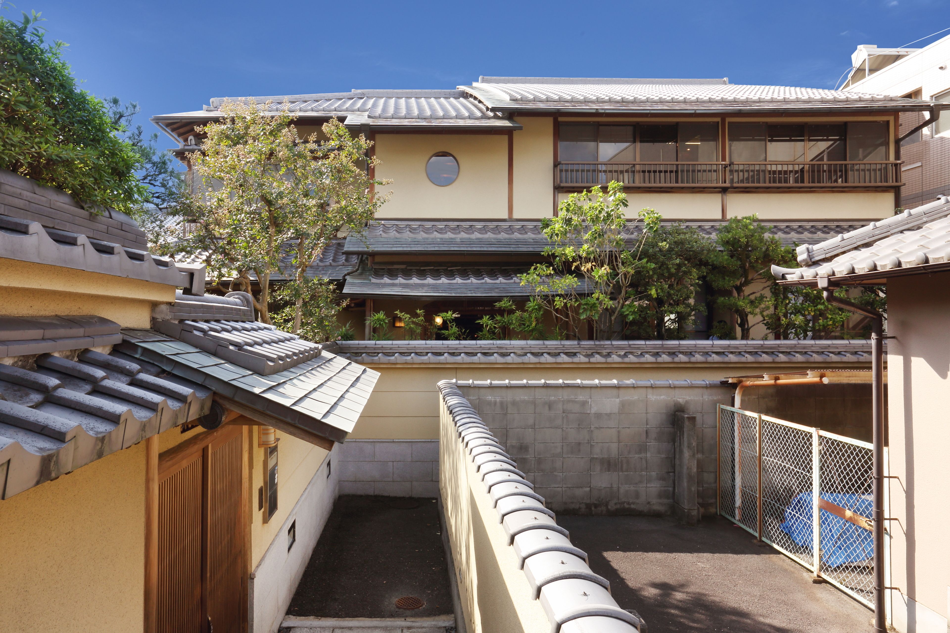 Un edificio japonés tradicional con tejado de tejas, un balcón de madera y un patio amurallado.