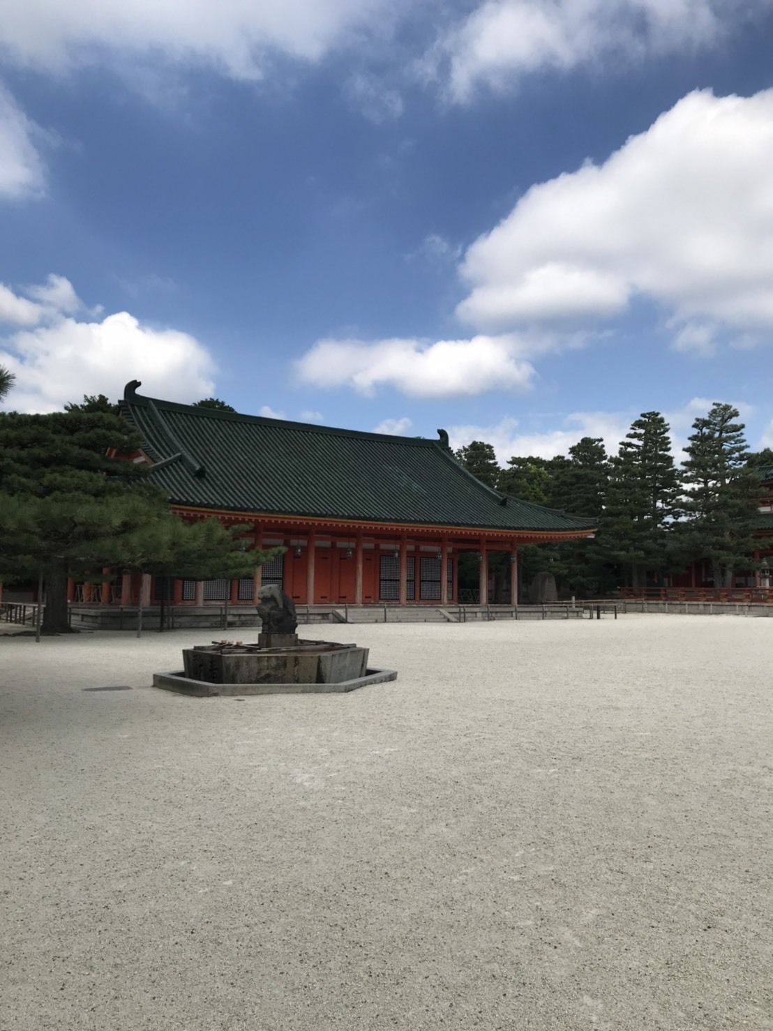 A traditional building with a tiled roof, surrounded by a gravel courtyard and trees.